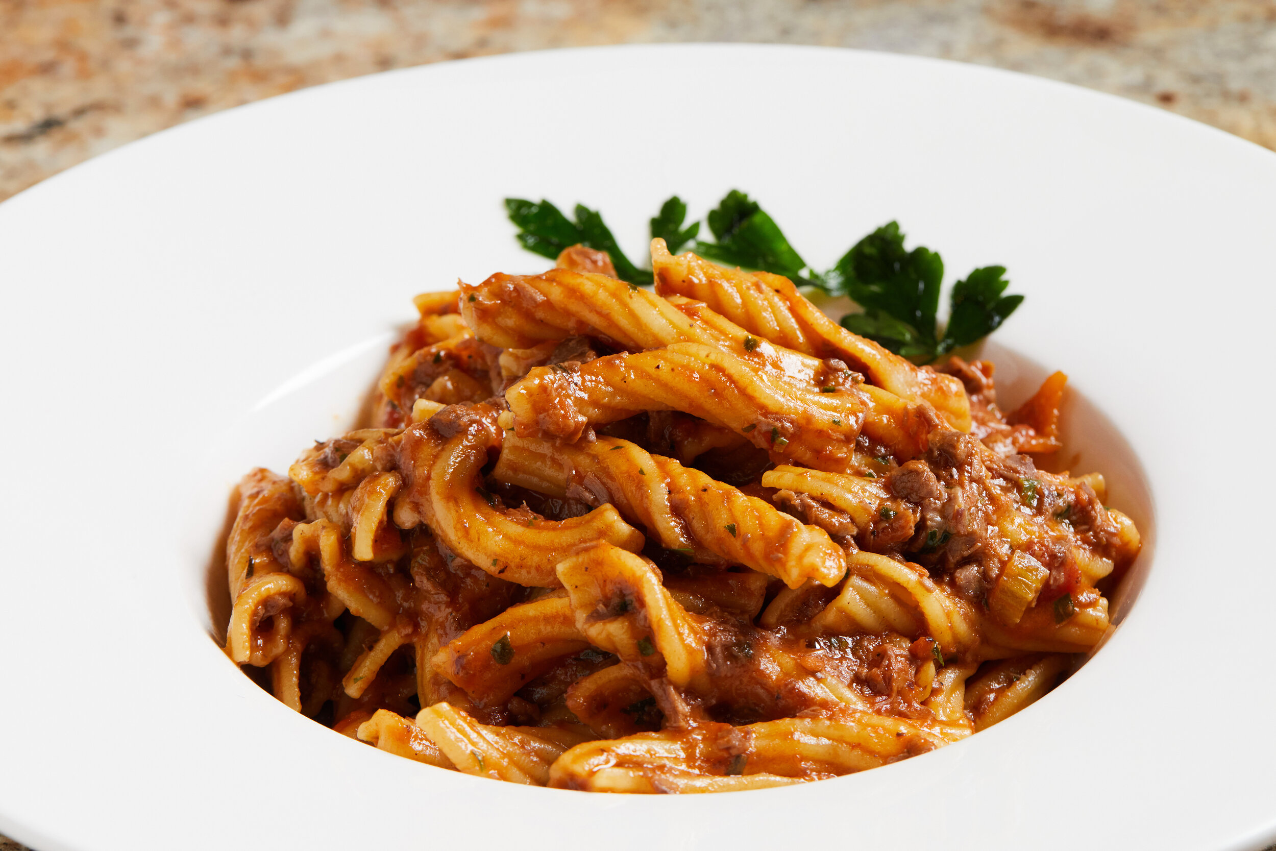 Plate of tagliatelle with meat sauce garnished with parsley.