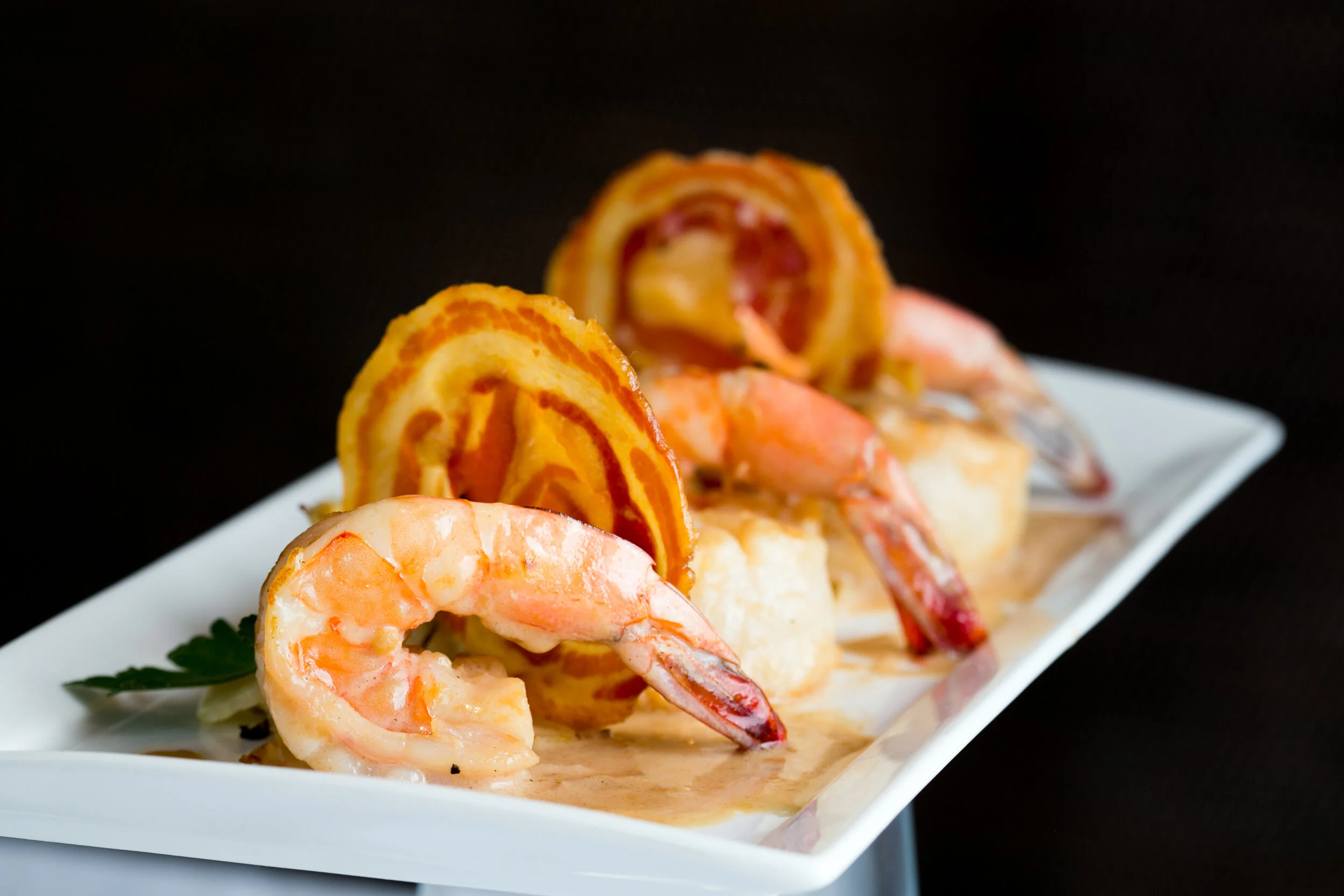 Shrimp and pancake bites topped with a swirl of fried onion rings served on a white rectangular plate