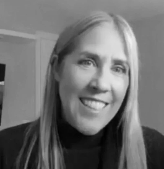 A woman with long hair smiling in front of a plain wall.