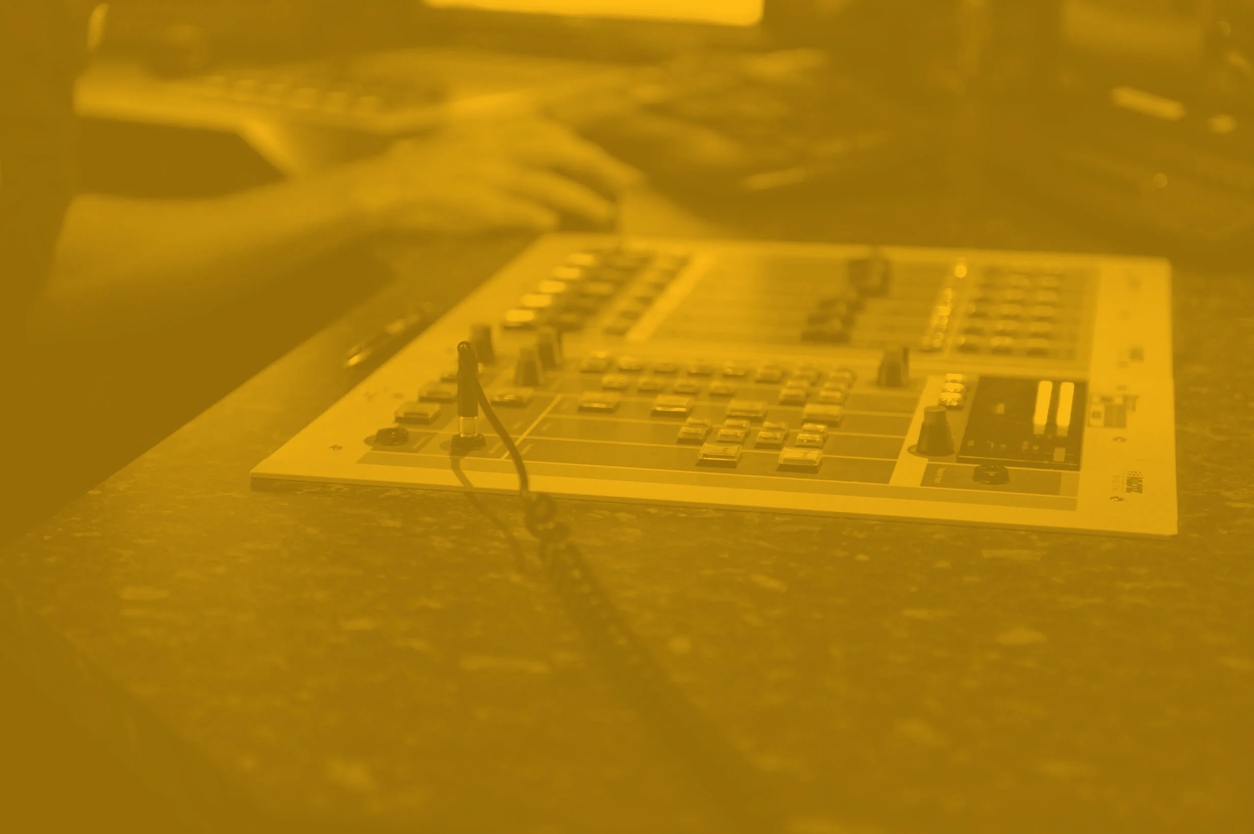 A sound mixing console with various sliders and knobs, blurred and yellow-tinted.