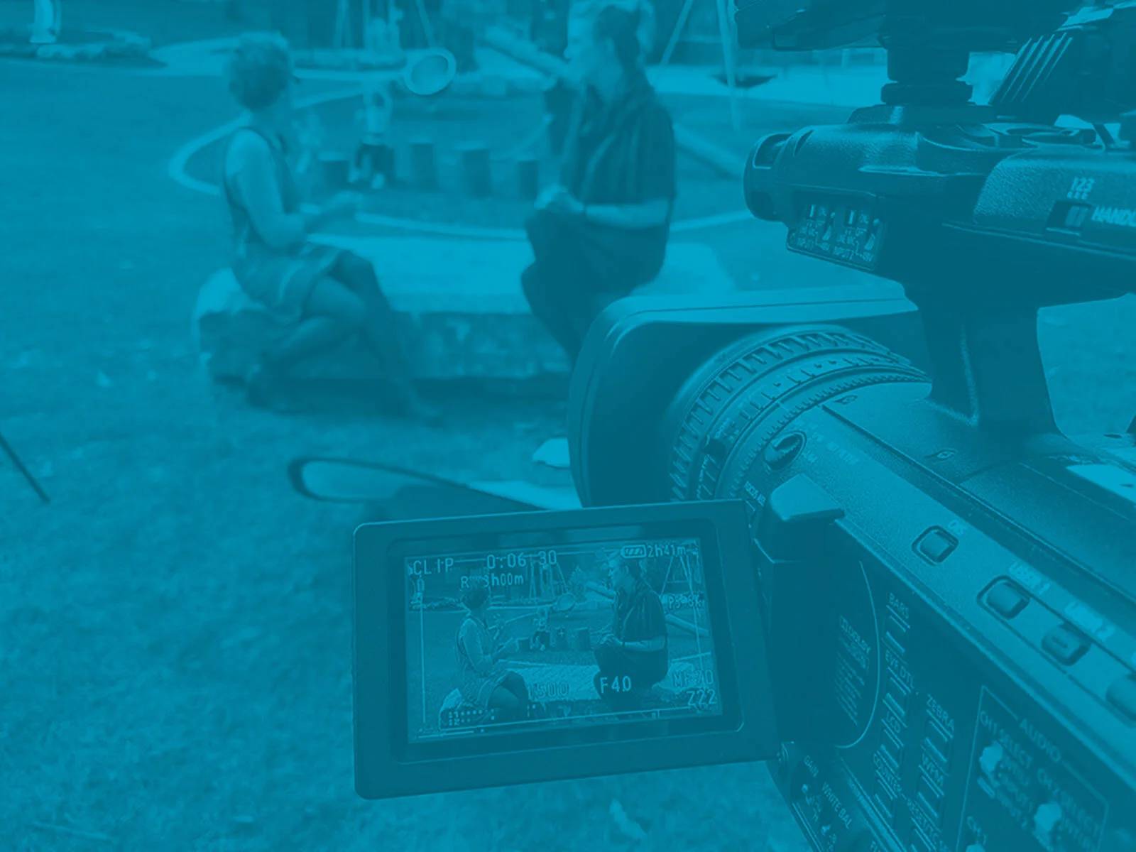Behind the scenes of a video recording session showing two children playing at a table outdoors, with a camera focused on the scene.