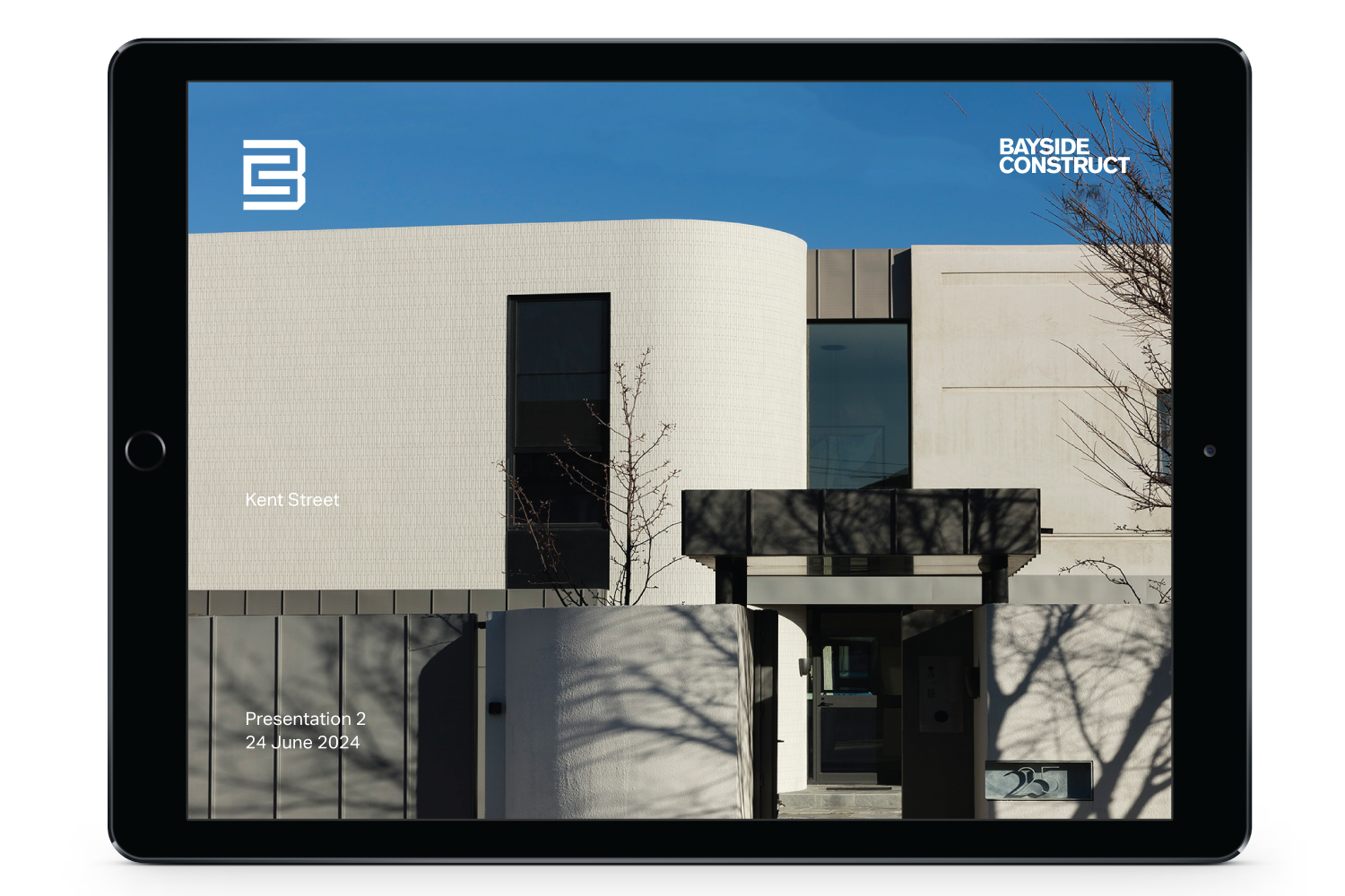 Tablet displaying a modern building with white walls, large windows, leafless trees, blue sky, and text indicating a presentation date of June 24, 2024.