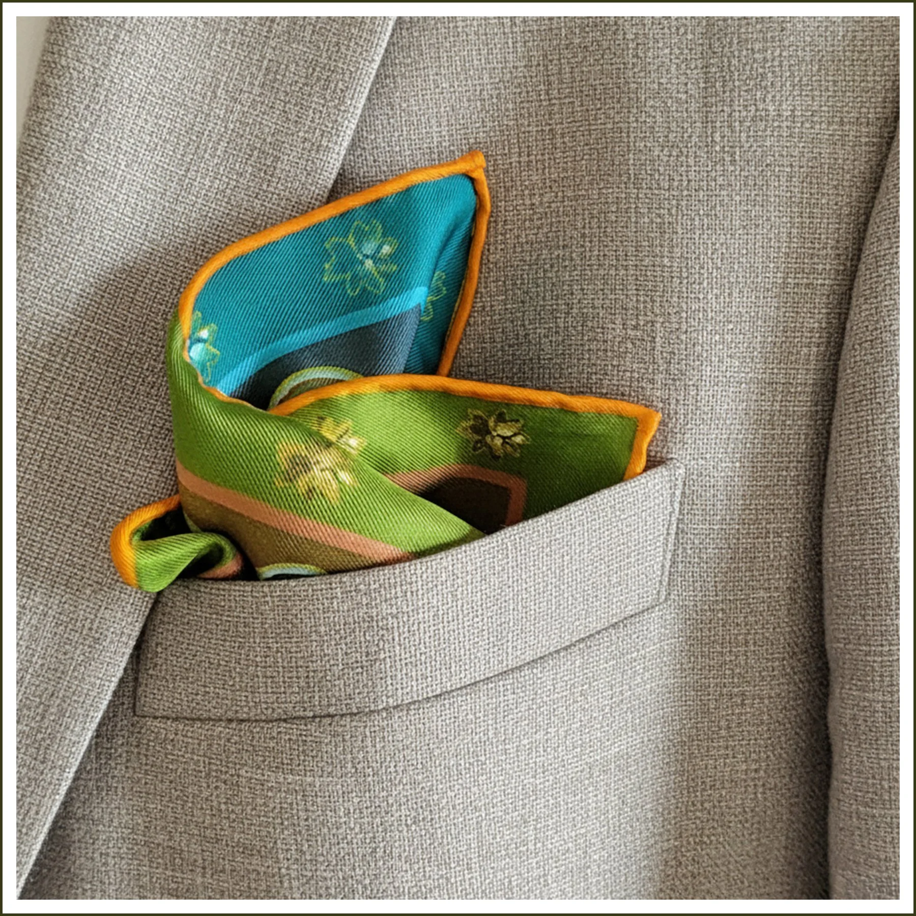 A colorful square pattern pocket square or neck scarf with teal. blue, green, gold designs featuring, florals.