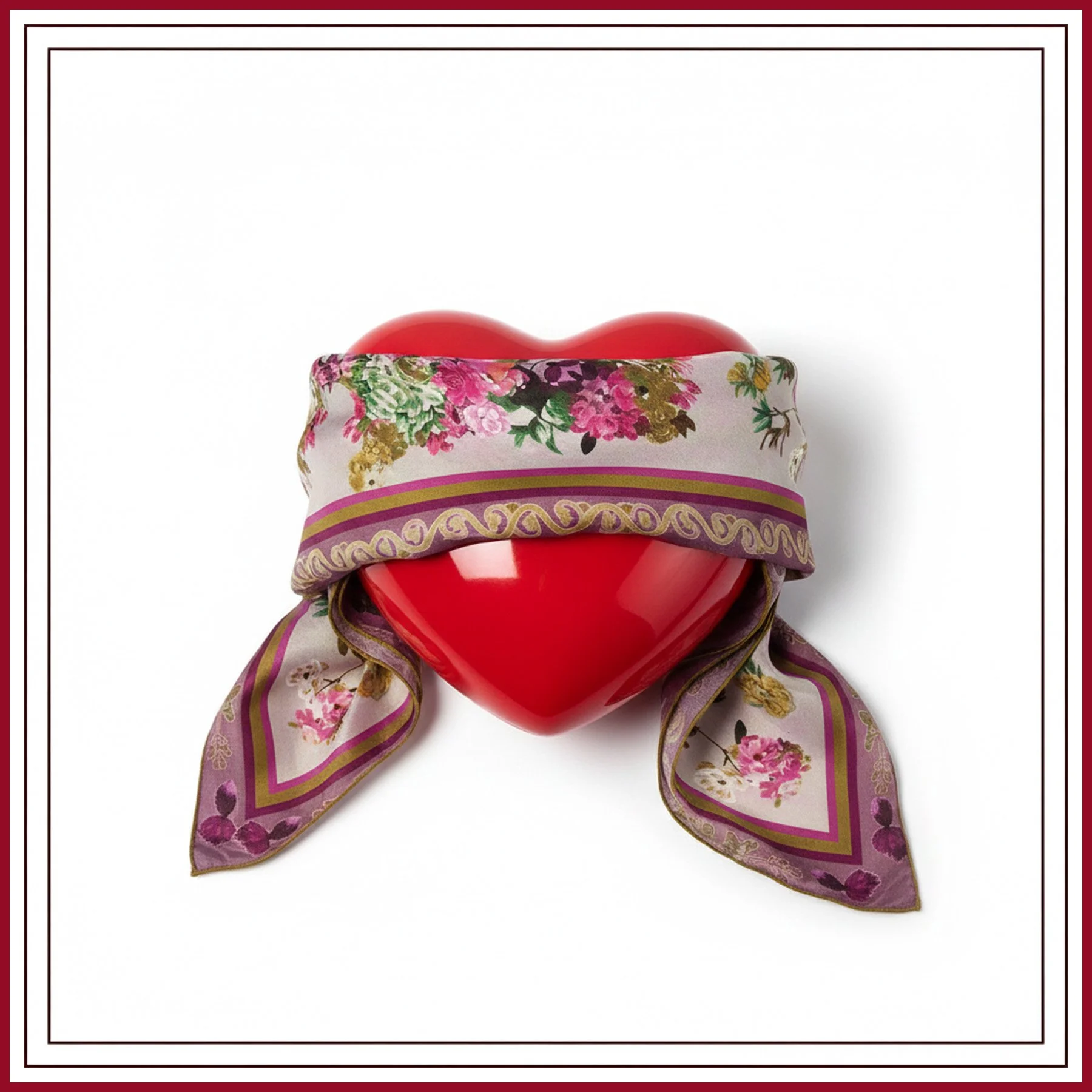 A red heart-shaped object wrapped with a colorful floral scarf that has purple, pink, and gold patterns.