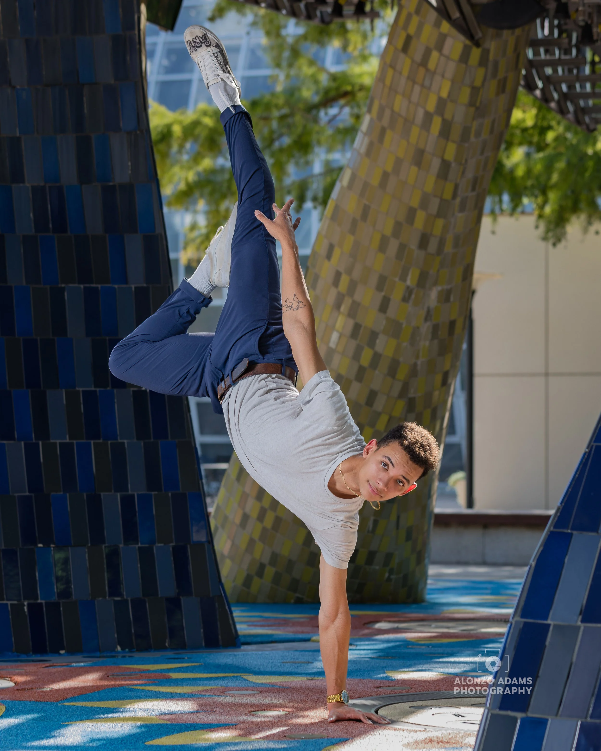 Male dancer in pants and t-shirt doing a one hand stand with leg pose