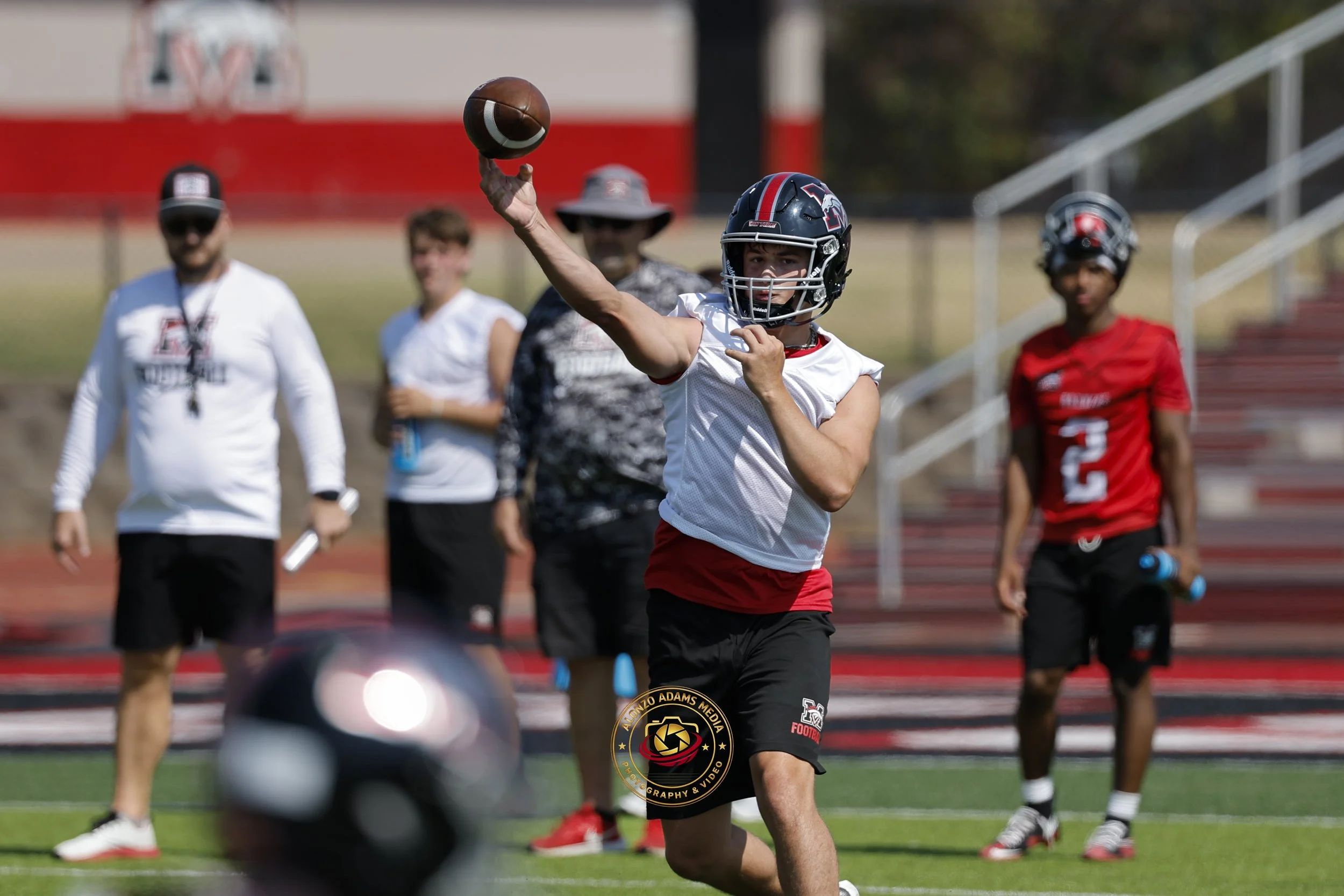 Mustang High School Football quarterback passes a ball wearing his helmet, jersey and shorts during fall practice.