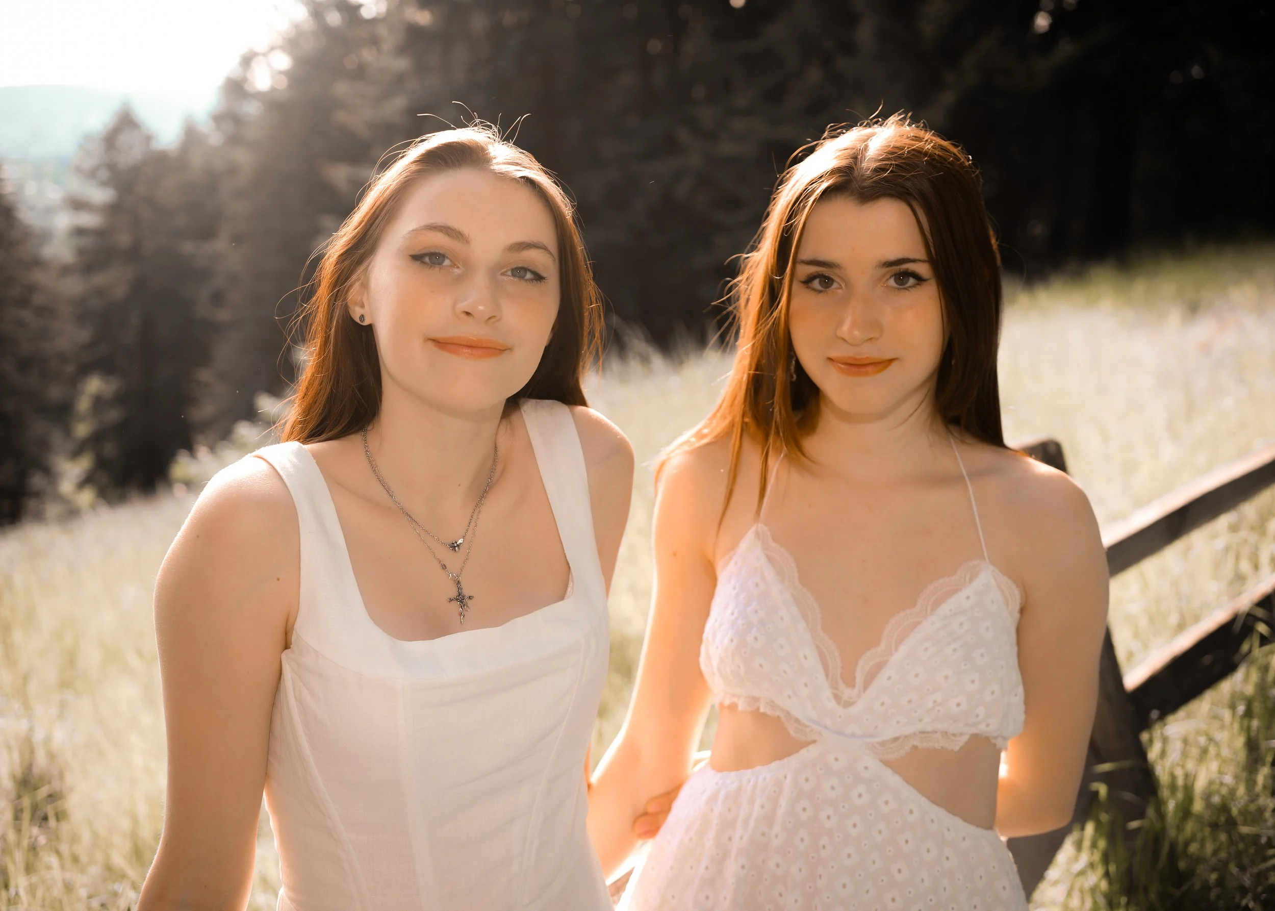 Two women in white dresses standing outdoors in a field with trees in the background.