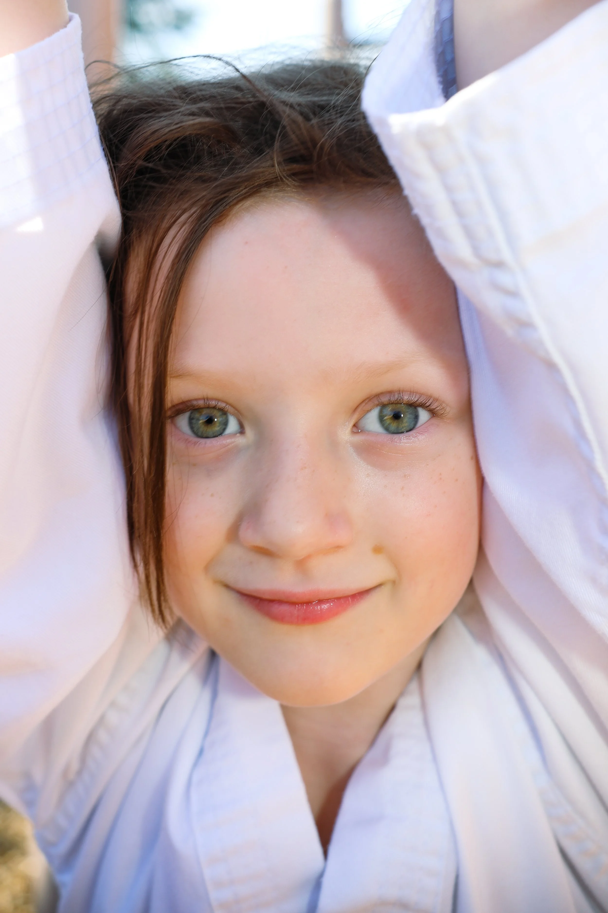 Smiling child wearing a white martial arts uniform with arms raised.
