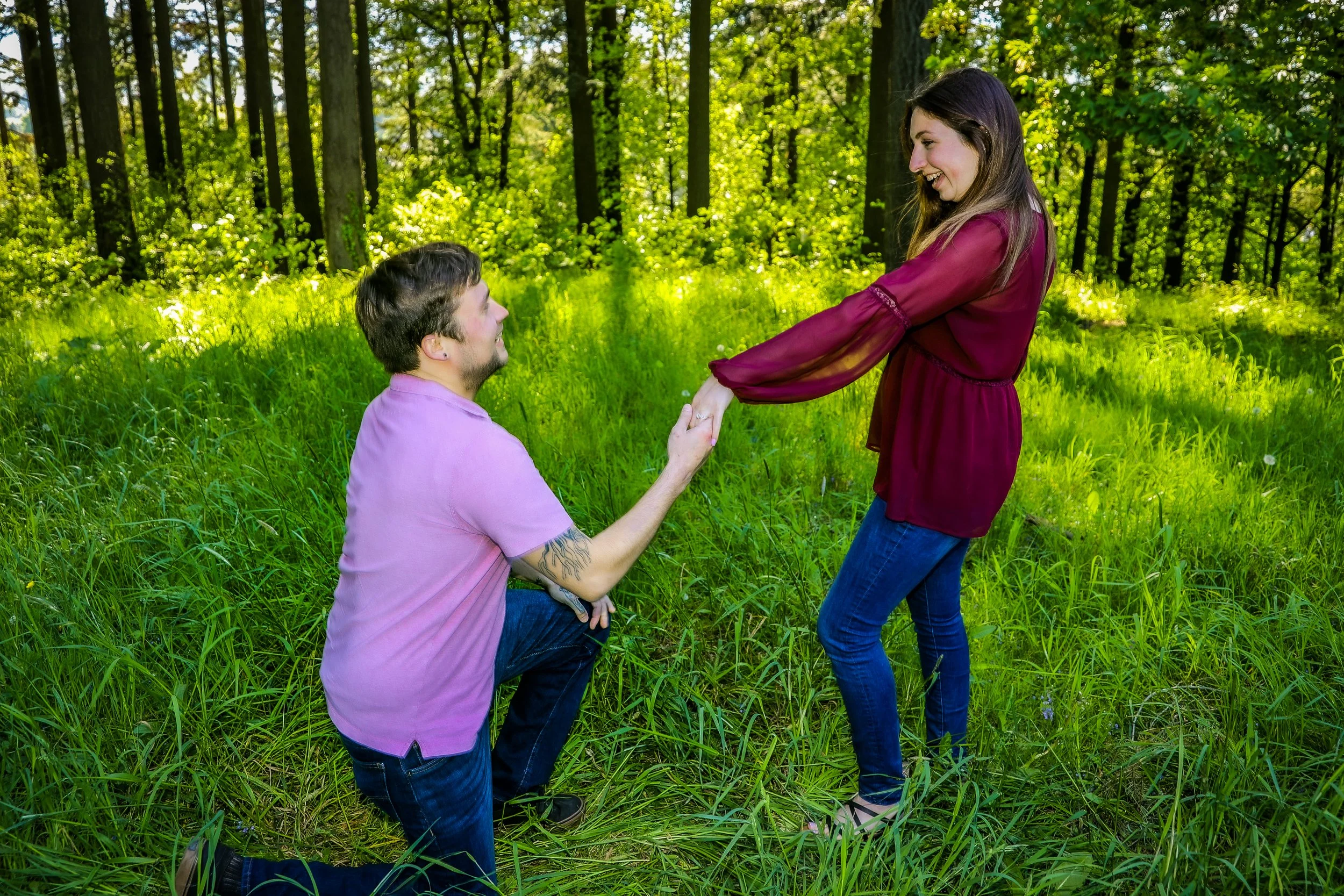 A man kneeling and proposing to a woman in a forest.