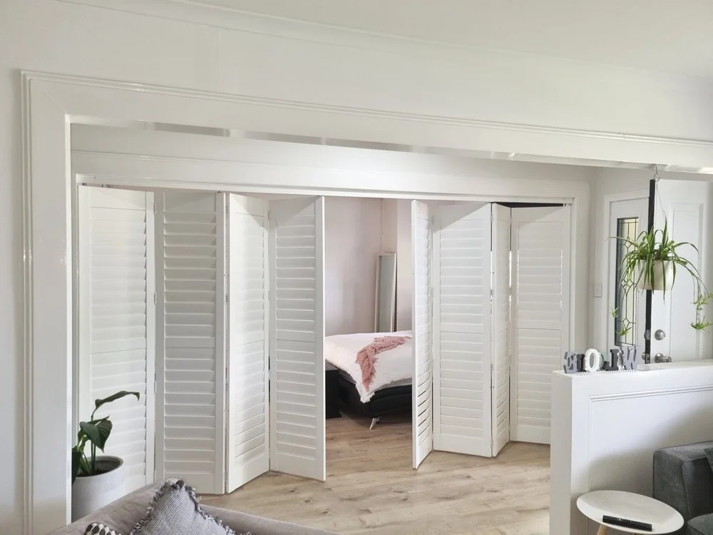 Living room with white plantation shutters, a white half-wall with decorative 'HOME' letters, a potted plant, and a gray couch with throw pillows.