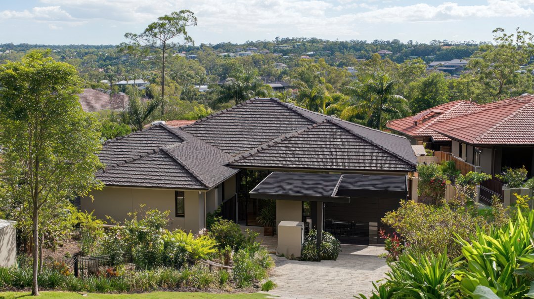 A view of a suburban house with a tiled roof surrounded by greenery and trees, with more houses and trees in the background.