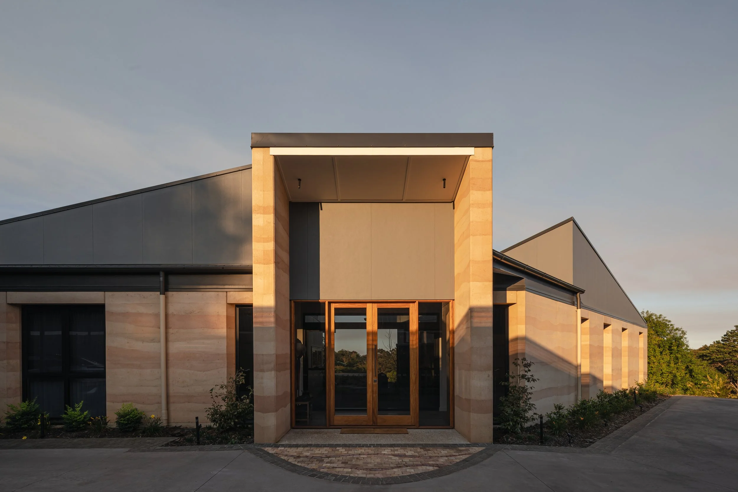 Modern building with a geometric design, large glass doors, and a flat roof, illuminated by warm sunset light.