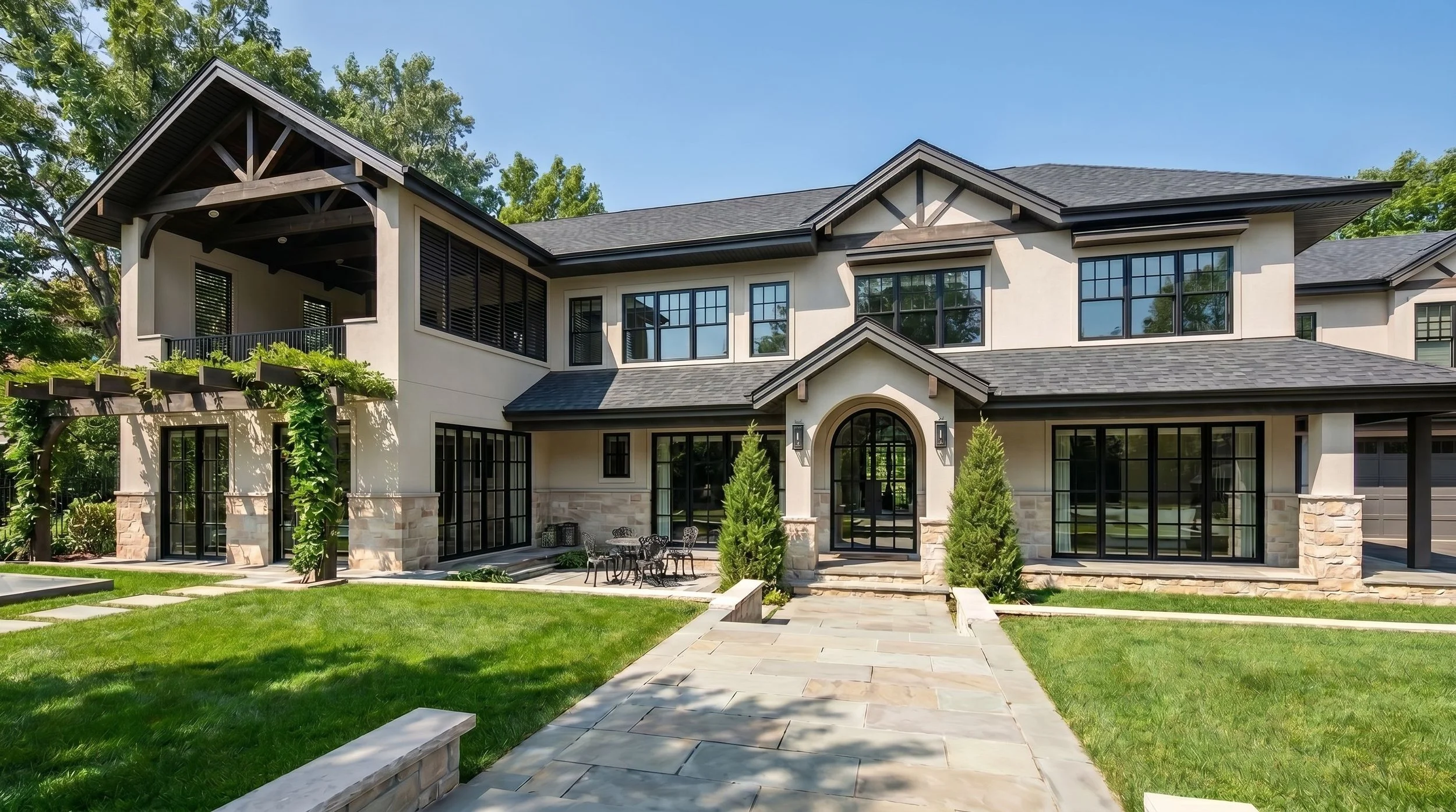 A modern, multi-story house with large windows, a balcony, surrounded by a well-maintained lawn and trees, with a stone pathway leading to the entrance.