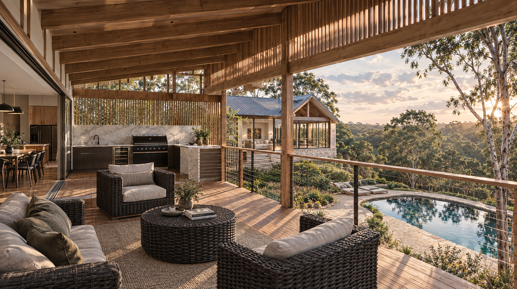 Outdoor living space on a wooden balcony with wicker furniture, a built-in kitchen, and a view of a swimming pool, trees, and a sunset.
