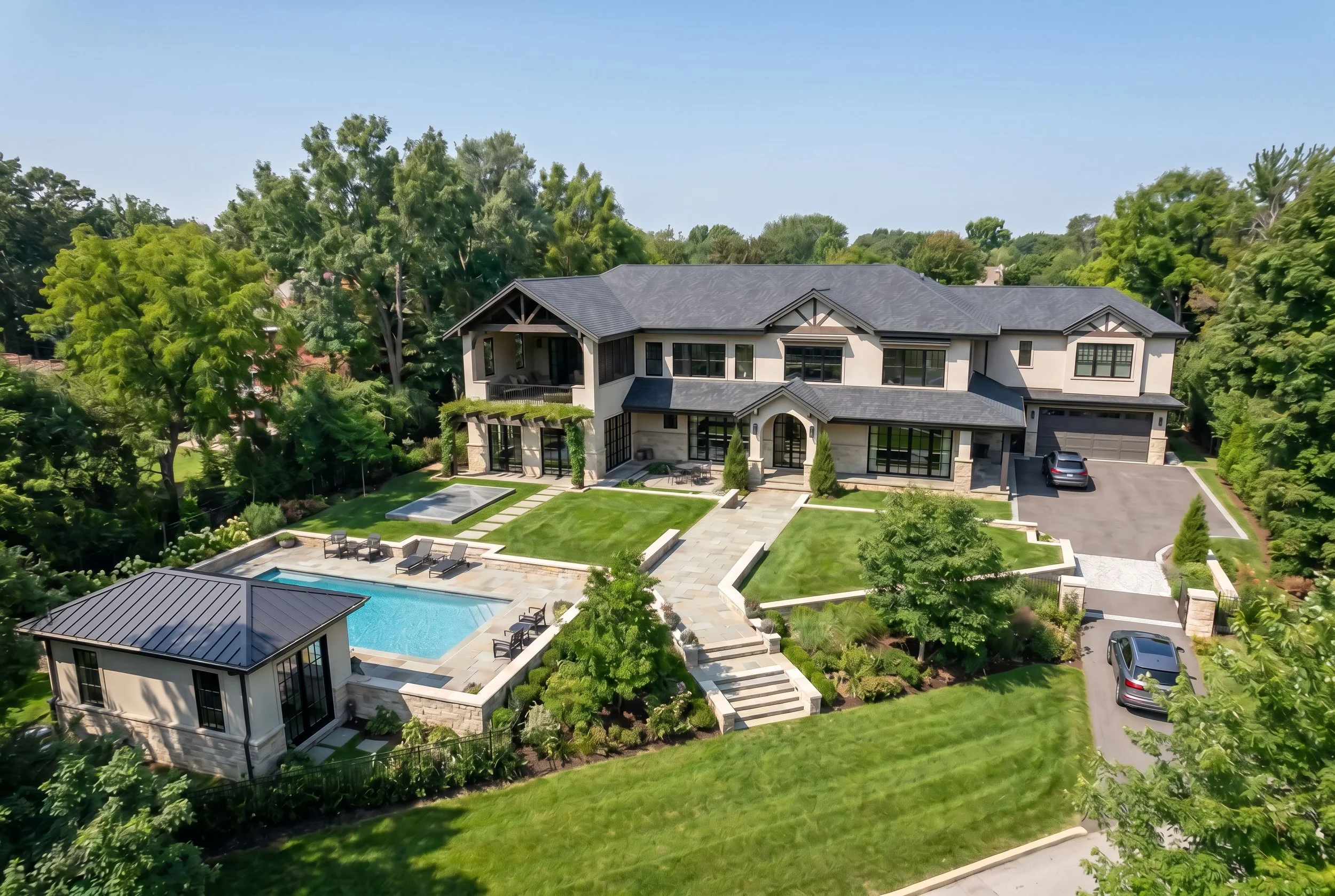 A large modern house with a backyard, swimming pool, outdoor seating, and lush green landscaping.