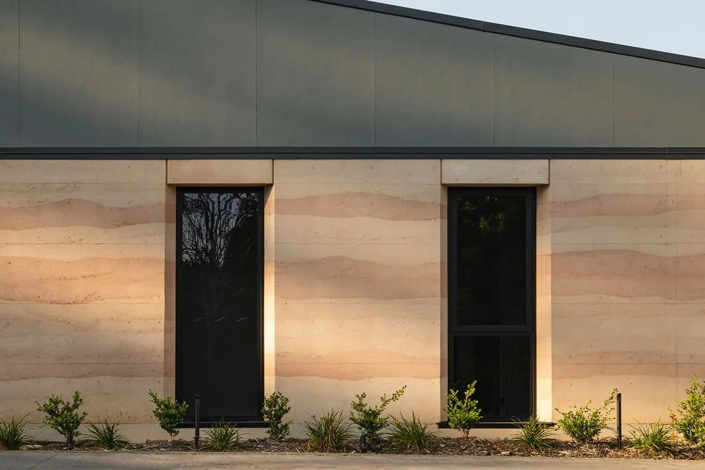 Modern building wall featuring two tall windows with greenery at the base.