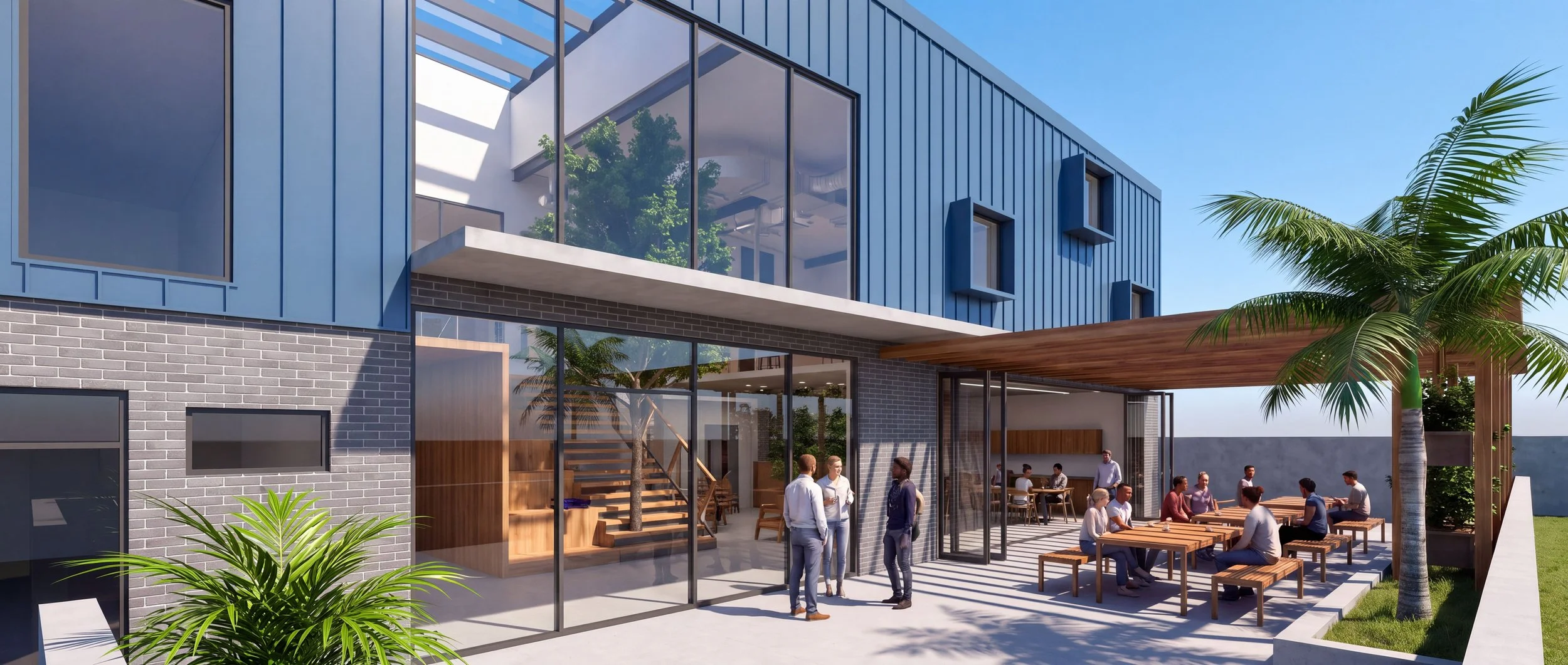 Modern multi-story building with blue exterior panels and large glass windows. There is an outdoor patio area with people sitting at wooden tables, some standing and talking. Palm trees are present around the patio, and the weather is sunny with a clear blue sky.
