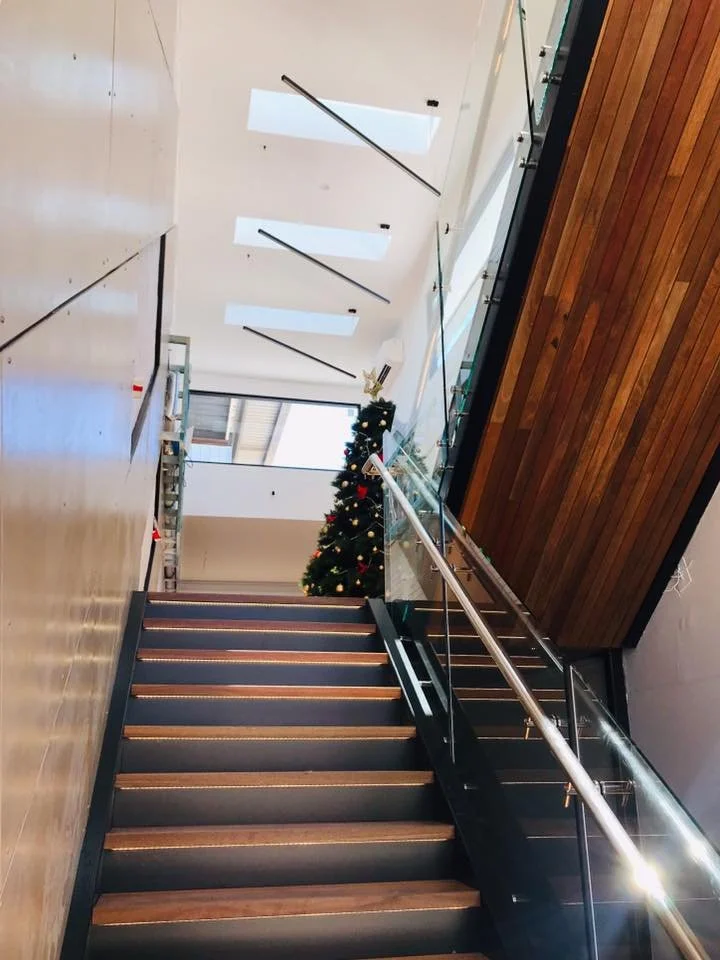 Interior of a modern building with a staircase, Christmas tree, and large windows.