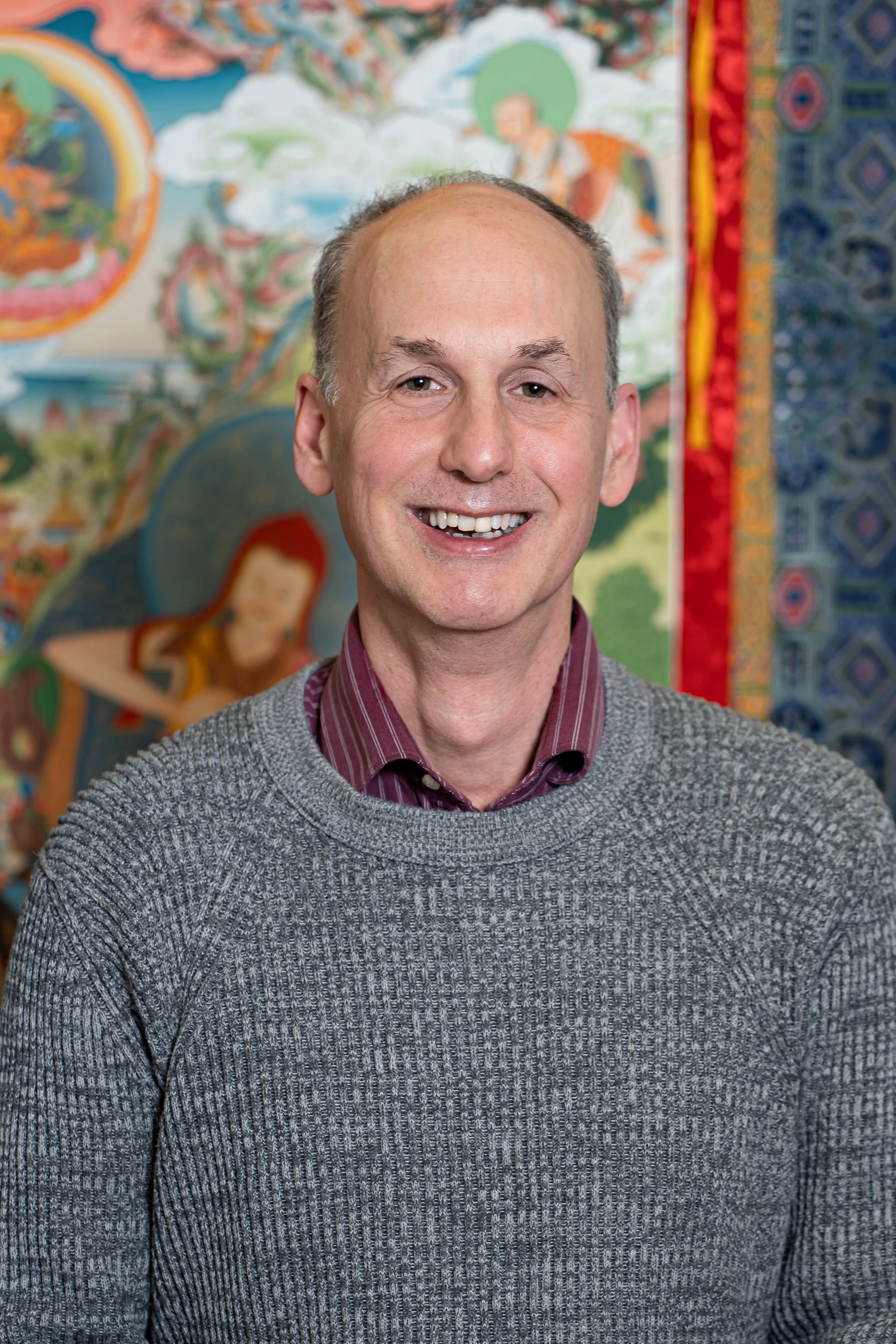 Man smiling, wearing a blue blazer and striped shirt, light background.