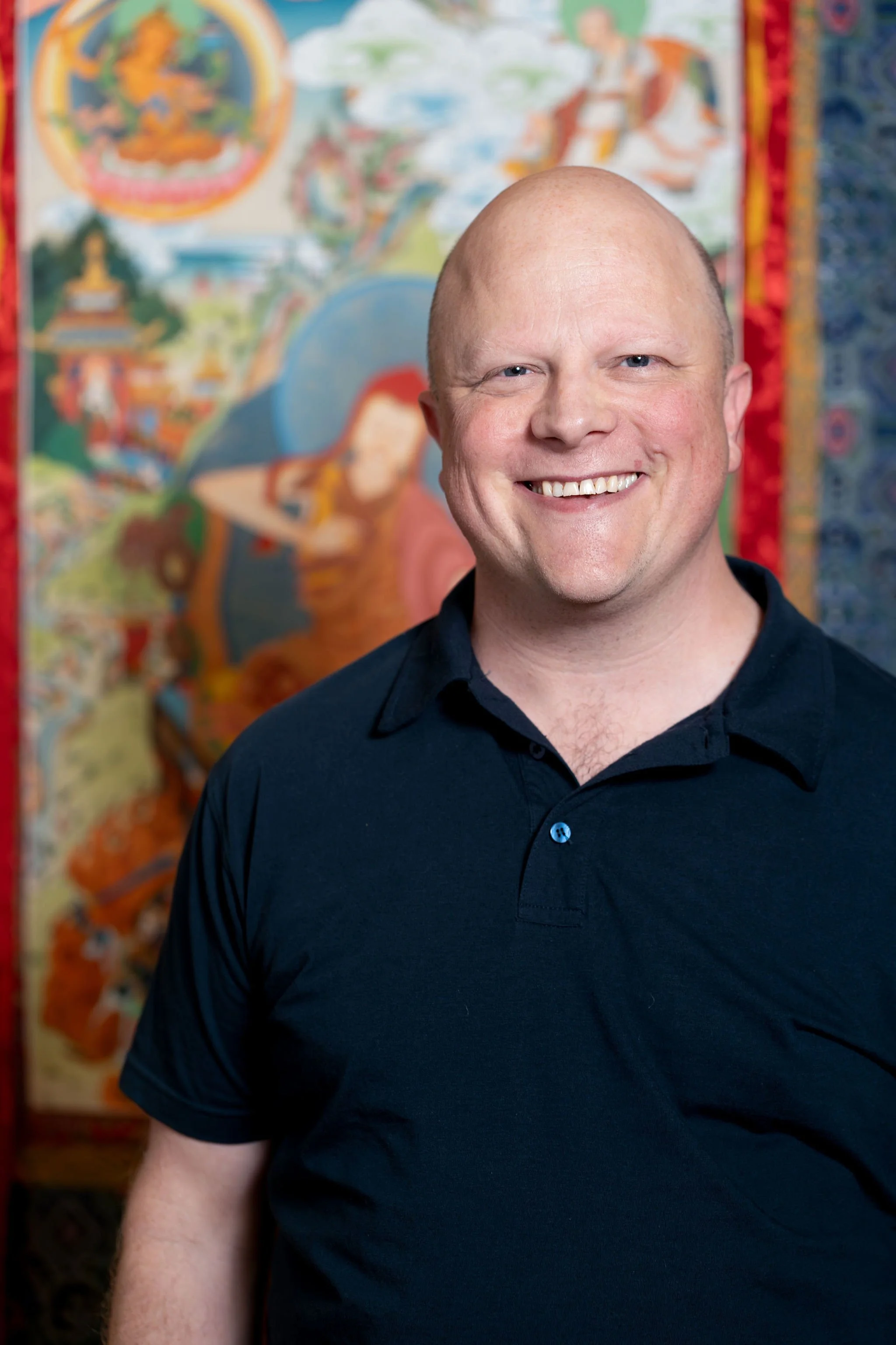 Smiling bald person wearing a black T-shirt with a white graphic.