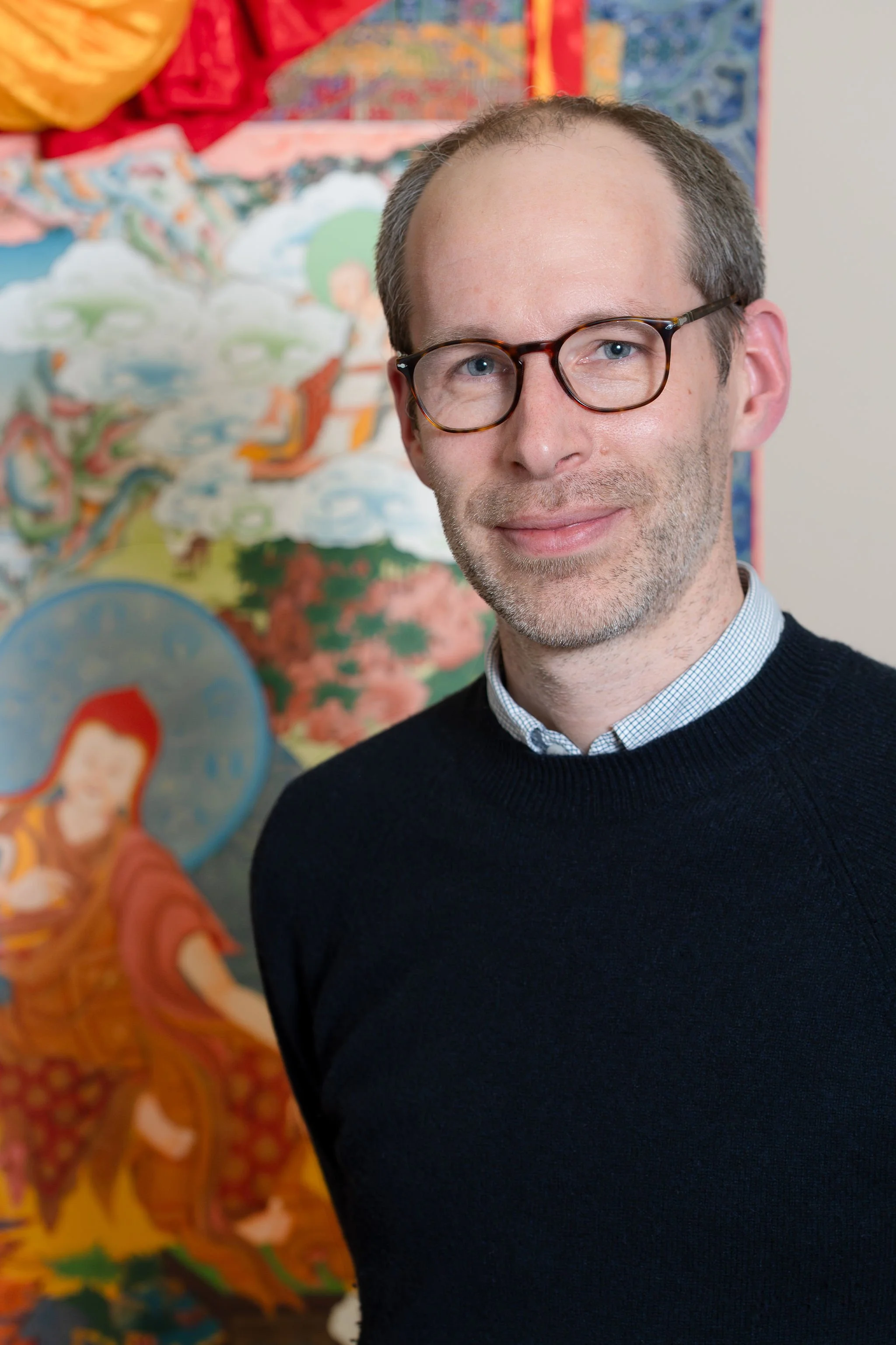 Man with glasses smiling in a blue shirt