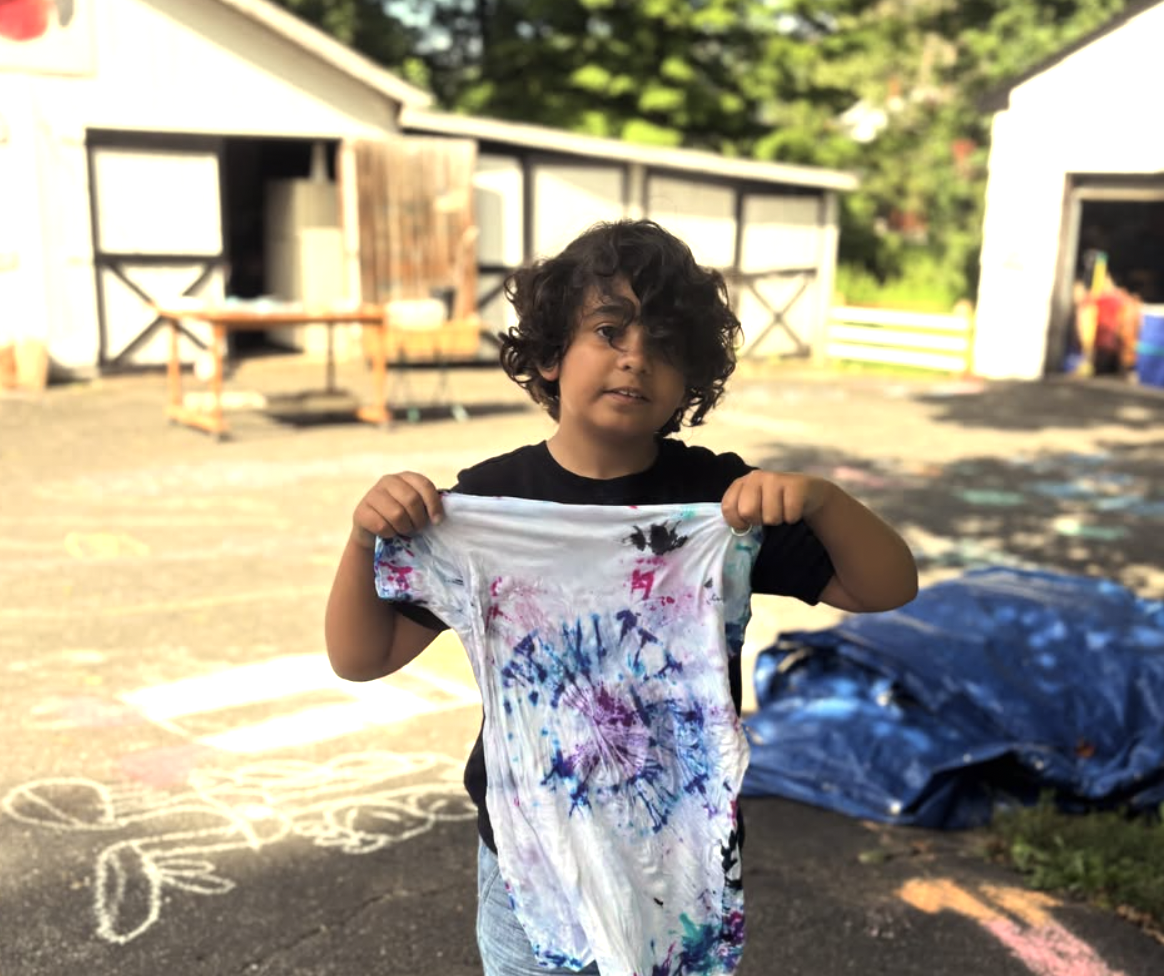 Young boy with curly hair holding a tied-dye T-shirt outdoors.