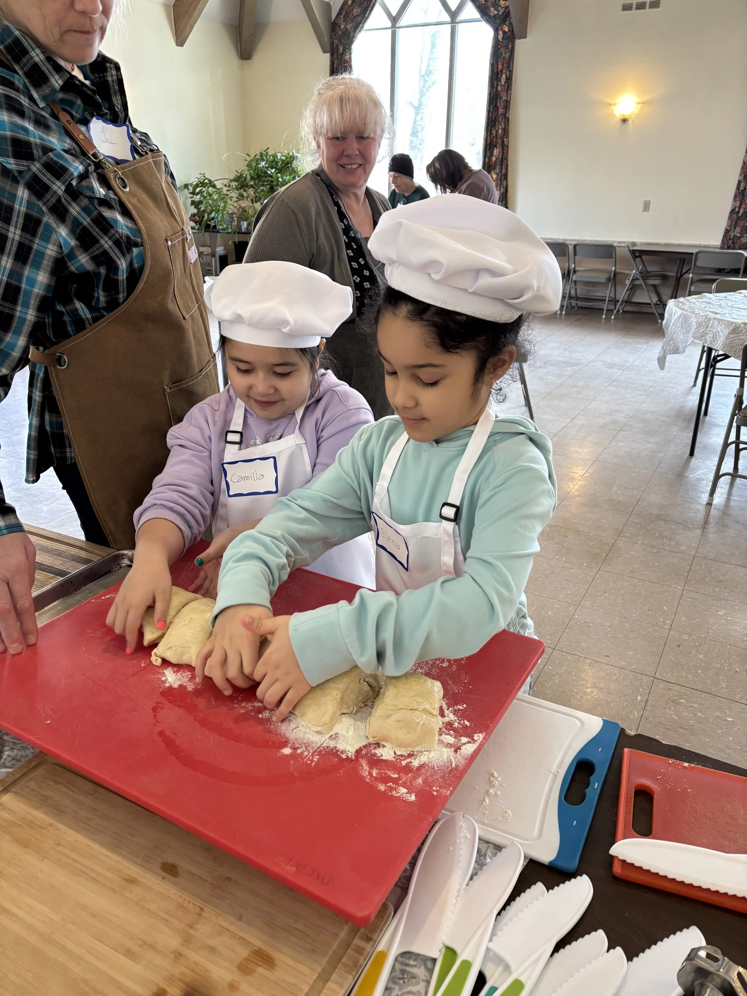 Two young girls enjoy learning how to roll out dough at M&J On The Way Farm, Inc Cooking Class for Kids