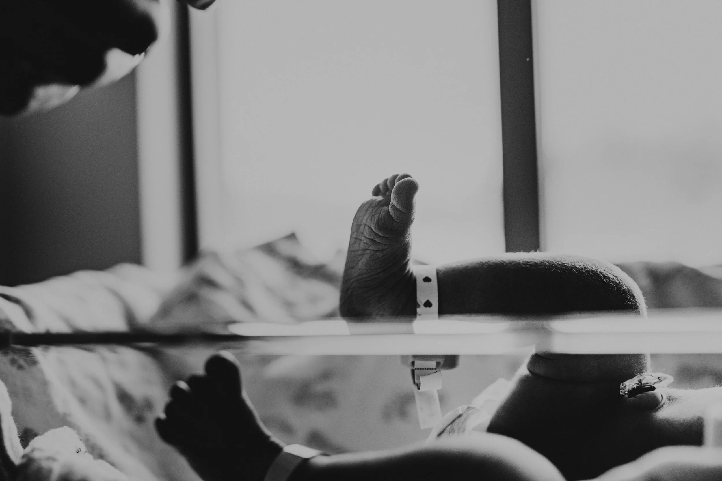 A person's hand and arm extending through a hospital bed rail, with a medical bracelet on the wrist, in a hospital room.