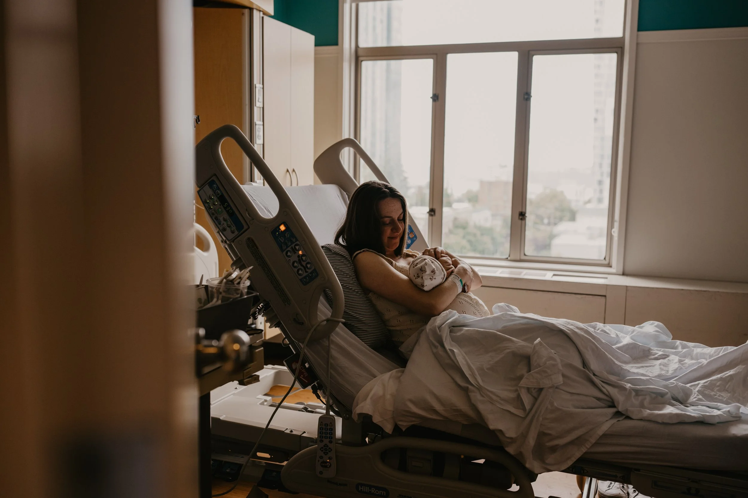 Mother holding and gazing at her newborn baby in hospital bed at Swedish First Hill documented by Elizabeth Anderson Photography Seattle