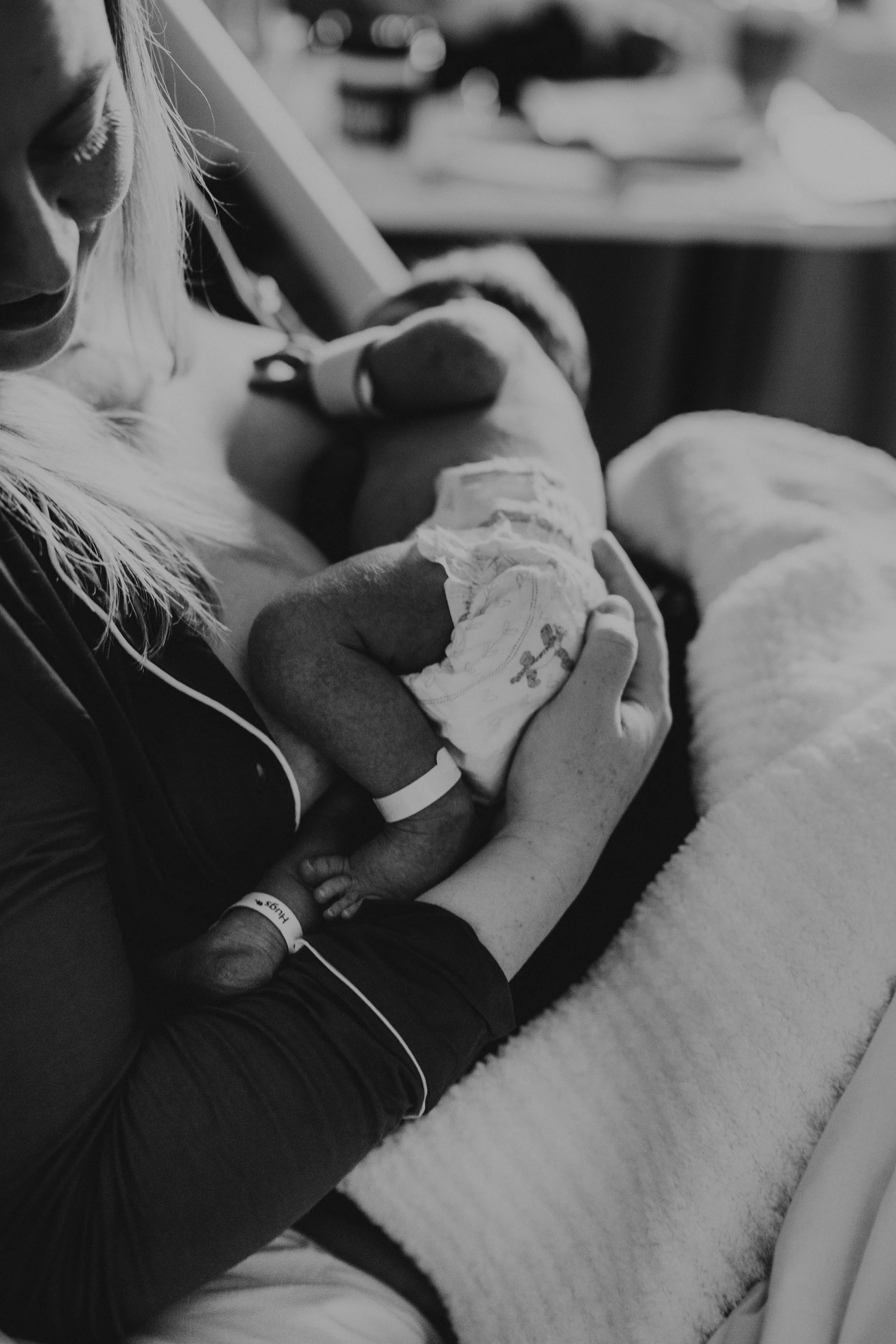 A woman holding a newborn baby in a hospital room, with a dog resting nearby.