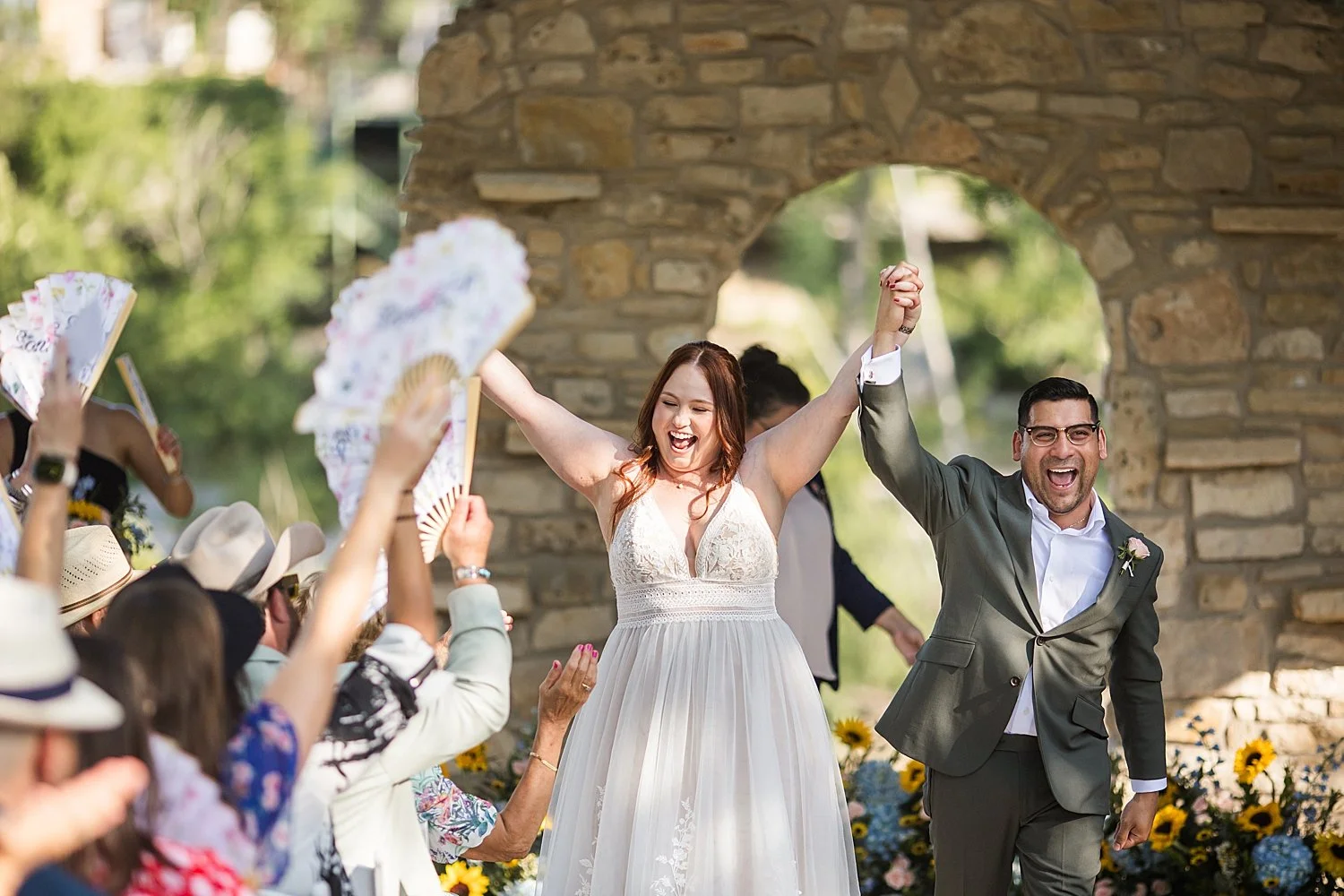 newlyweds throw up their hands in celebration by Dripping Springs Wedding Photographer