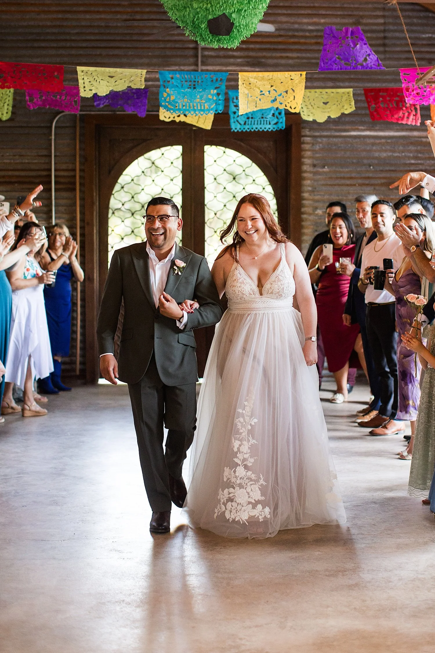 man and woman enter their reception under celebratory flags by Dripping Springs Wedding Photographer