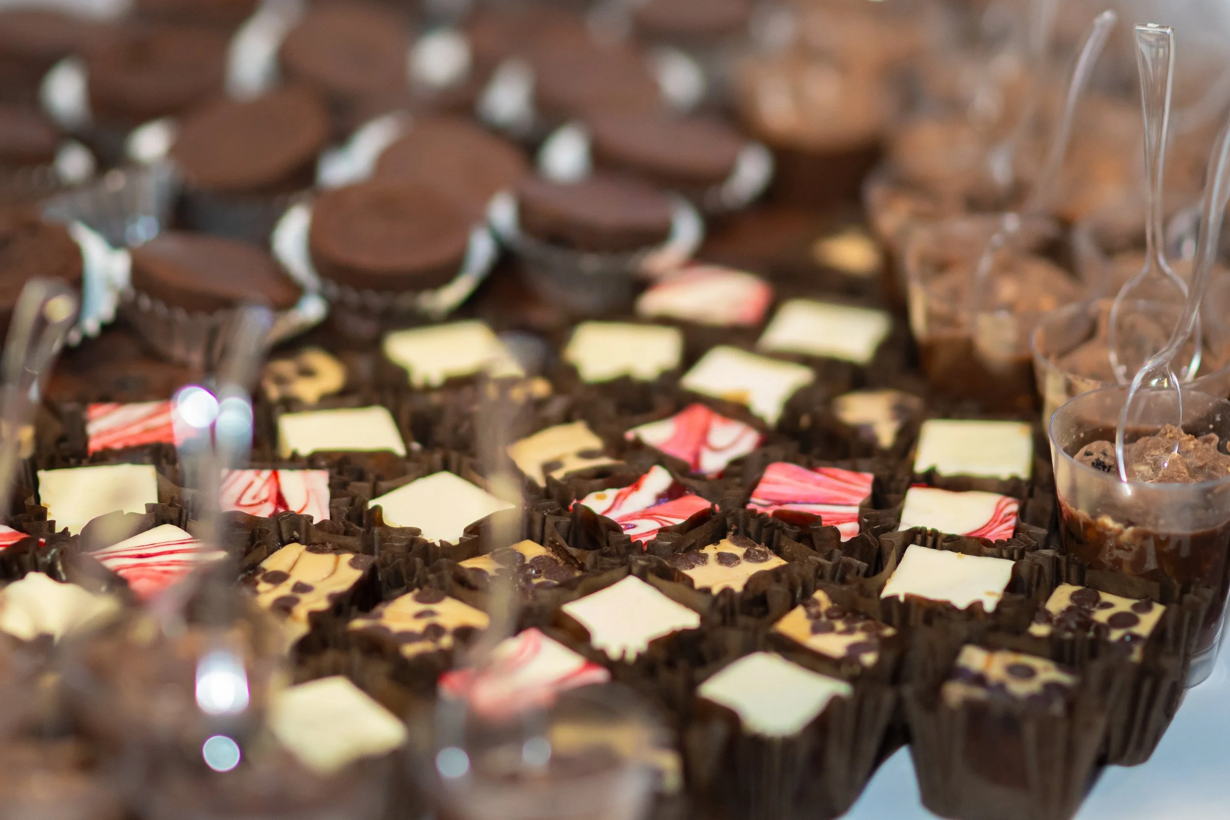 Assorted chocolates and desserts on a table, including chocolate cups and small glass cups filled with chocolate mousse with spoons.