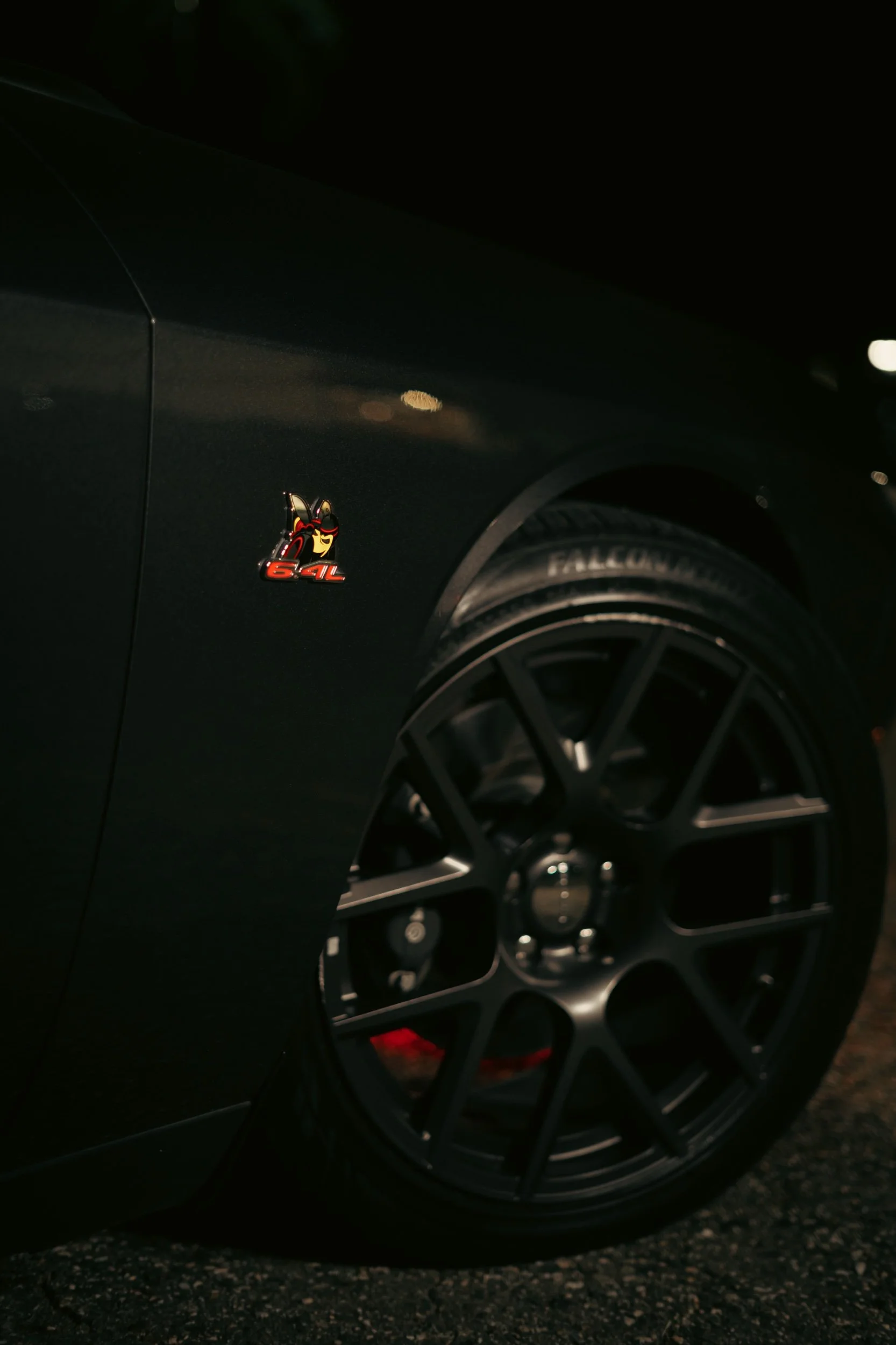 Close-up of a black car with a 'Detective Dog' emblem and a '64L' badge on the side, featuring a black wheel with a futuristic spoke design.