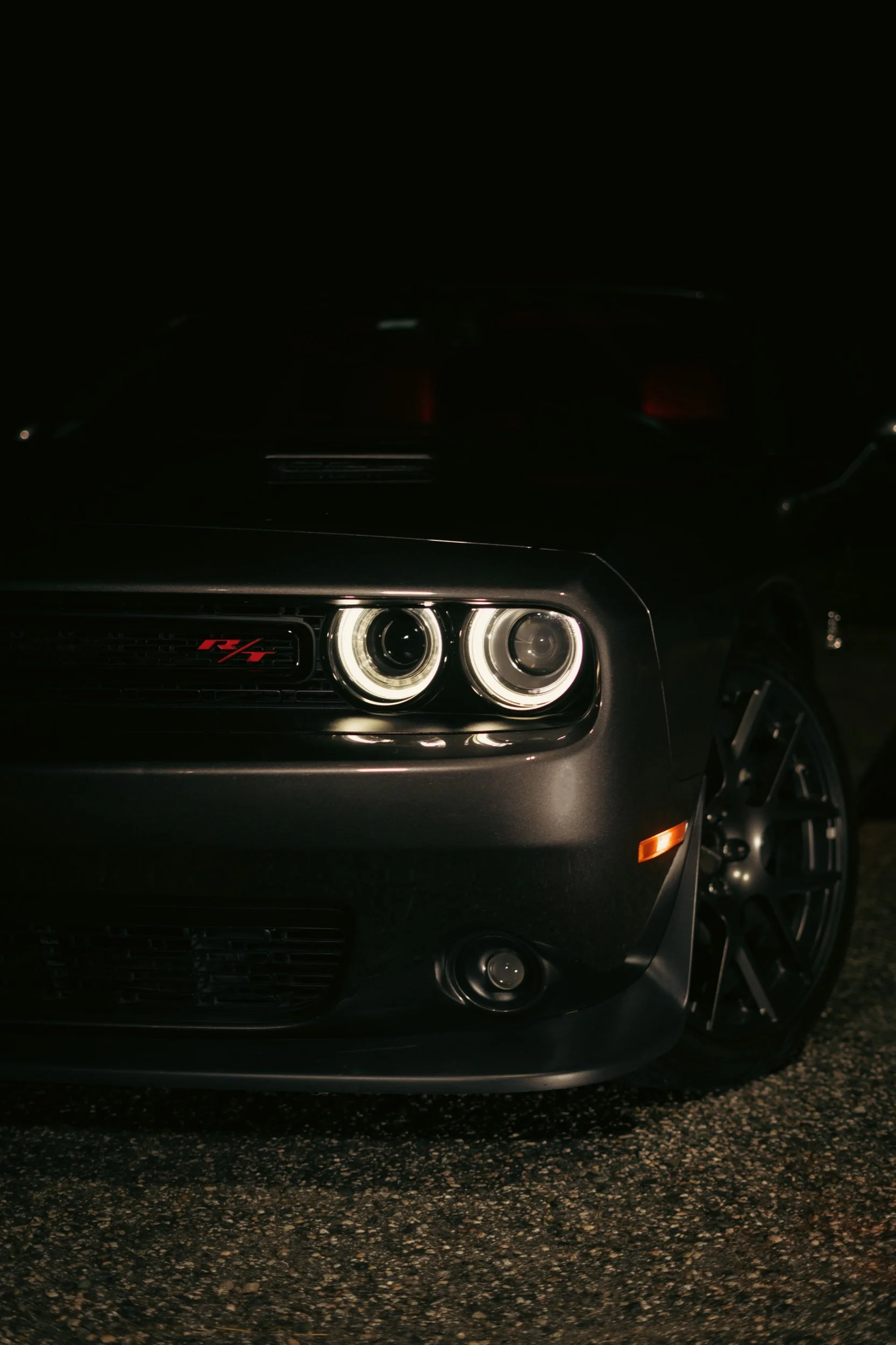Close-up of a black Dodge Charger with R/T badge at night, showing front headlight and wheel.
