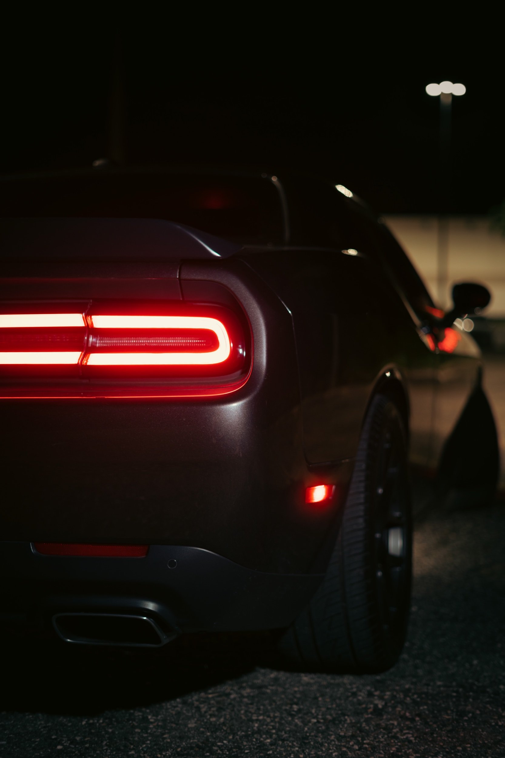 Rear view of a black sports car at night with illuminated taillights and a dark background.