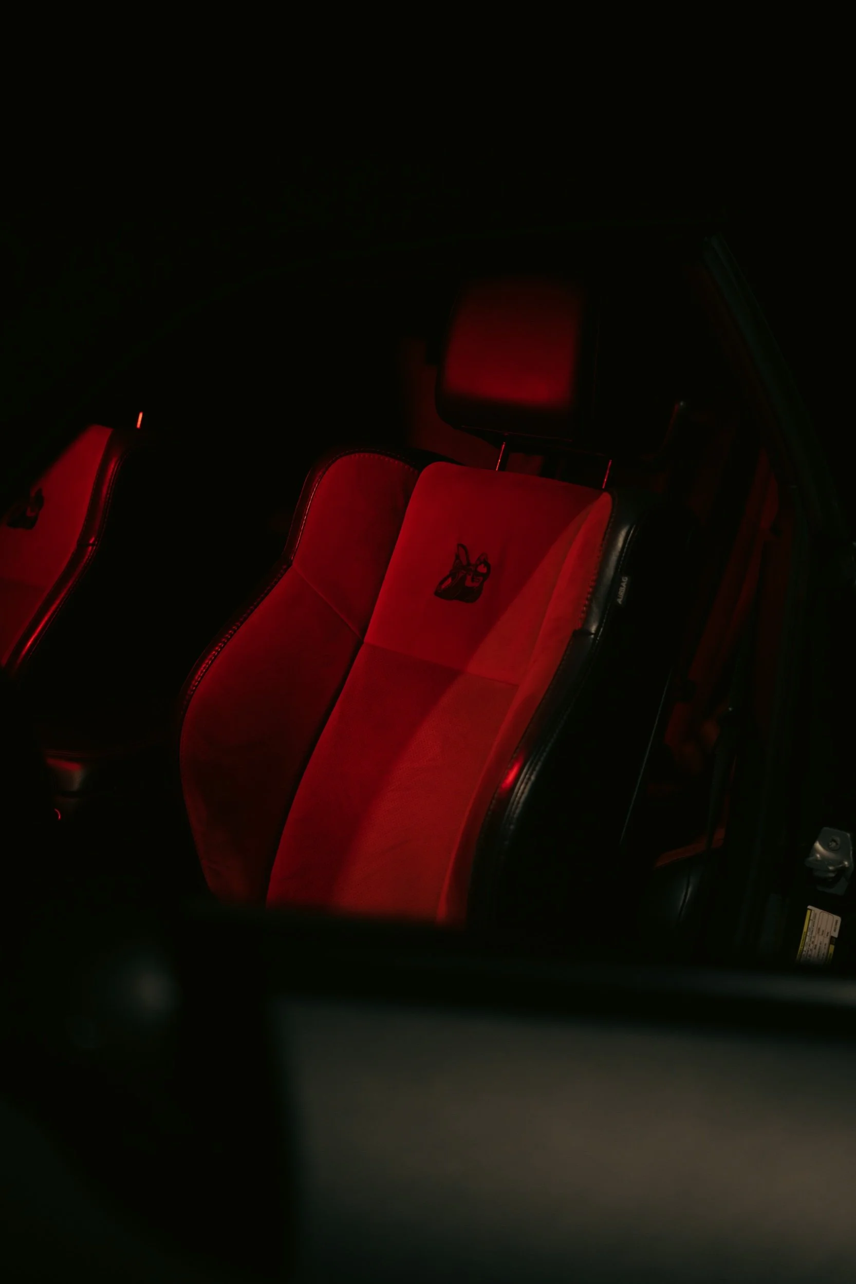 Car interior with red seats and embroidered logo, dark lighting.