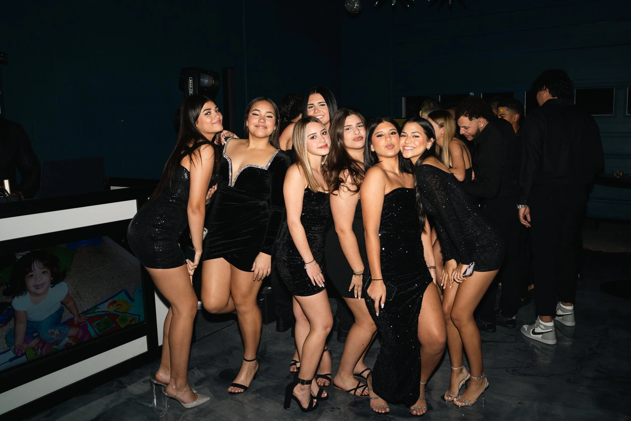 Group of young women in black dresses at a party, posing and smiling for the camera.