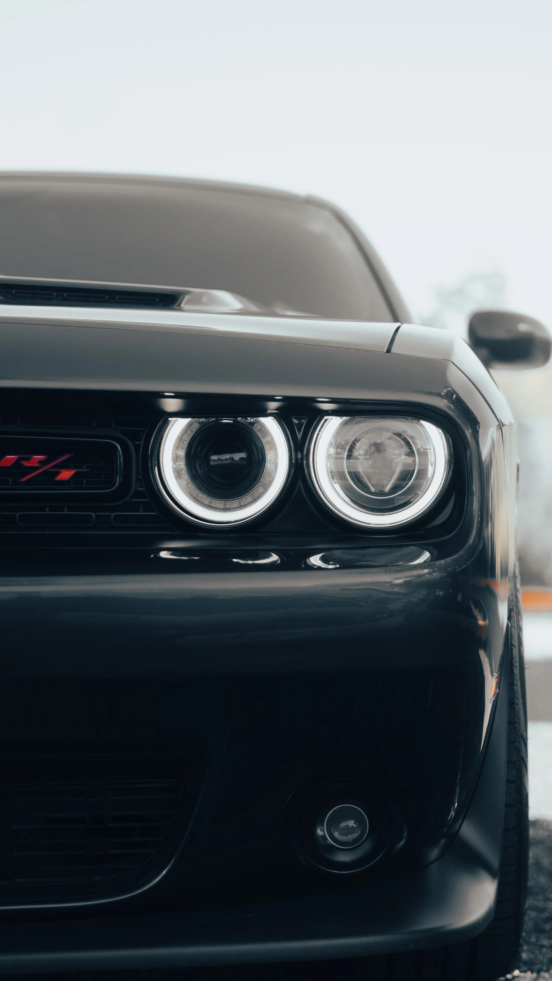 Close-up of the front end of a black Dodge Challenger with distinctive headlights and a red 'R/T' badge.