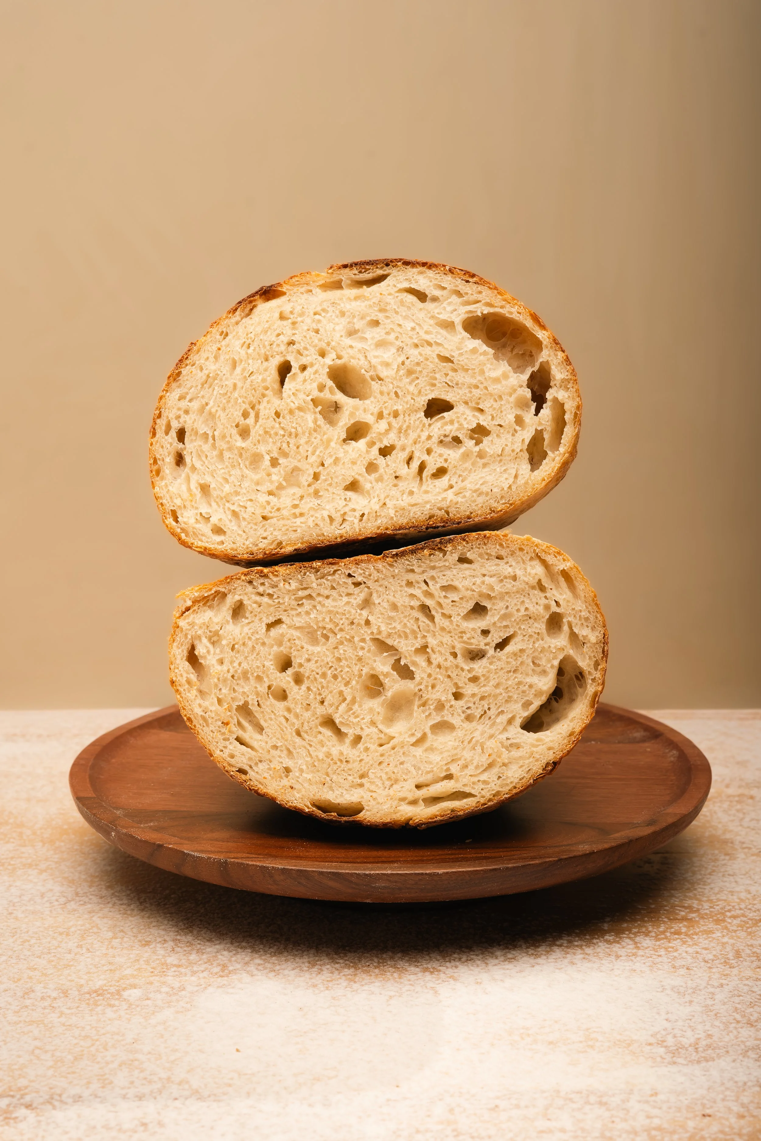 Close-up of two slices of bread stacked on a round wooden plate on a beige textured surface.