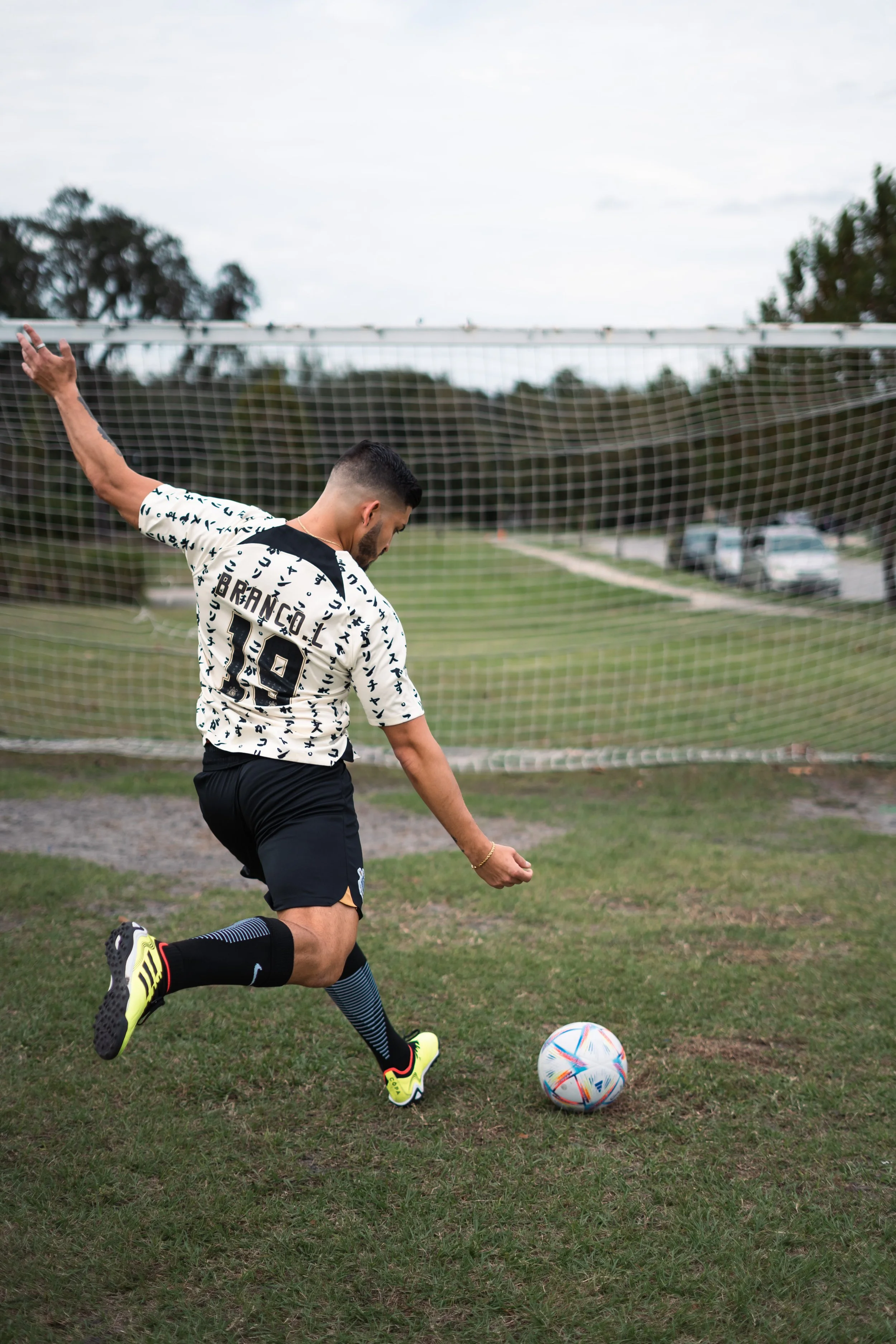 A soccer player kicking a ball on a grass field with a goal in the background.