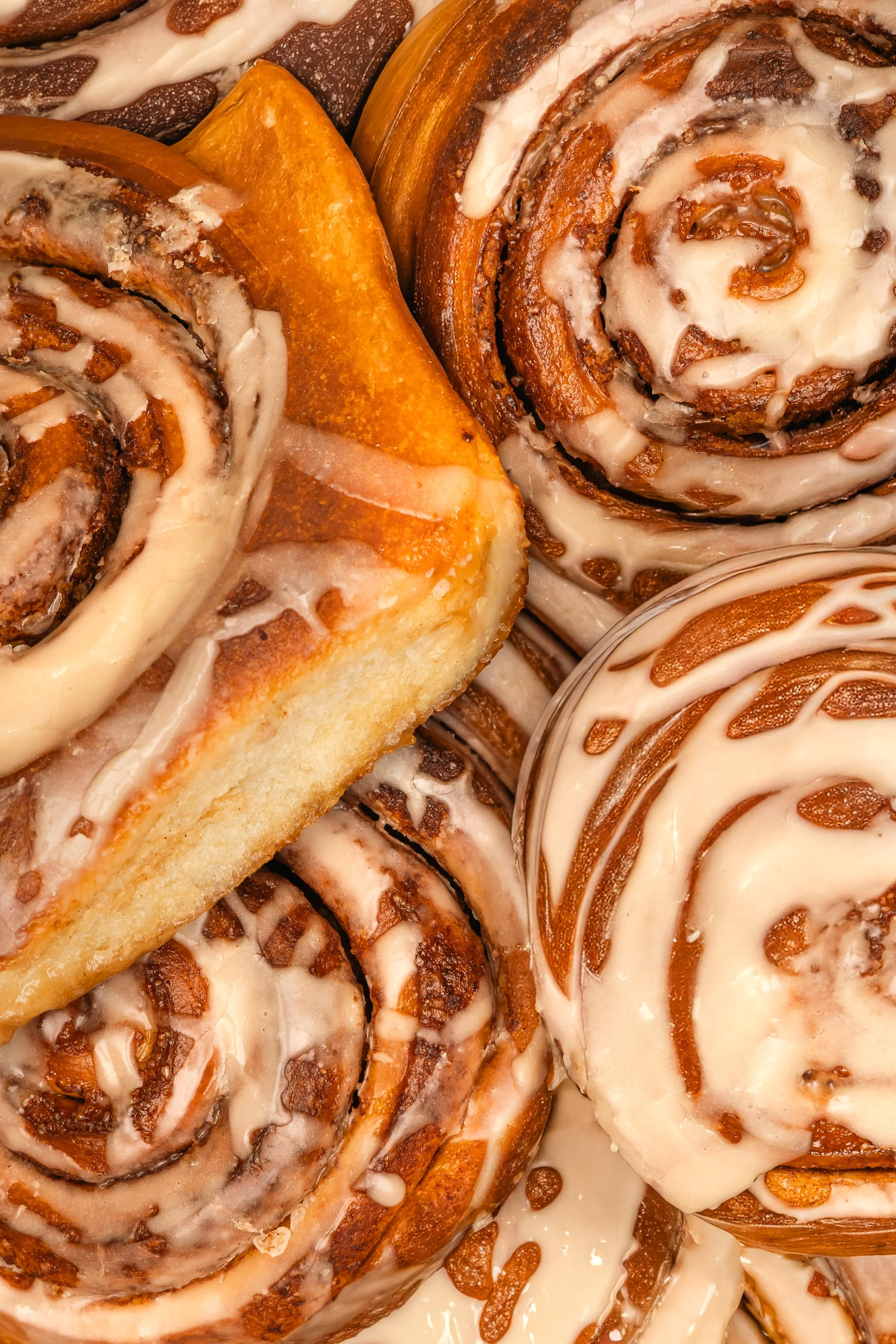 Close-up of cinnamon rolls topped with white icing, some drizzled with caramel and others with white icing.