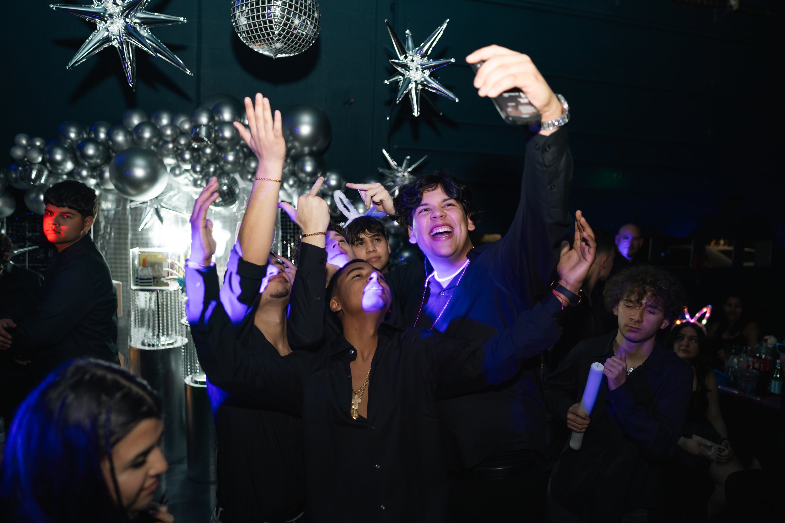People celebrating at a party with metallic balloons and decorations, taking a selfie, and enjoying the festive atmosphere.