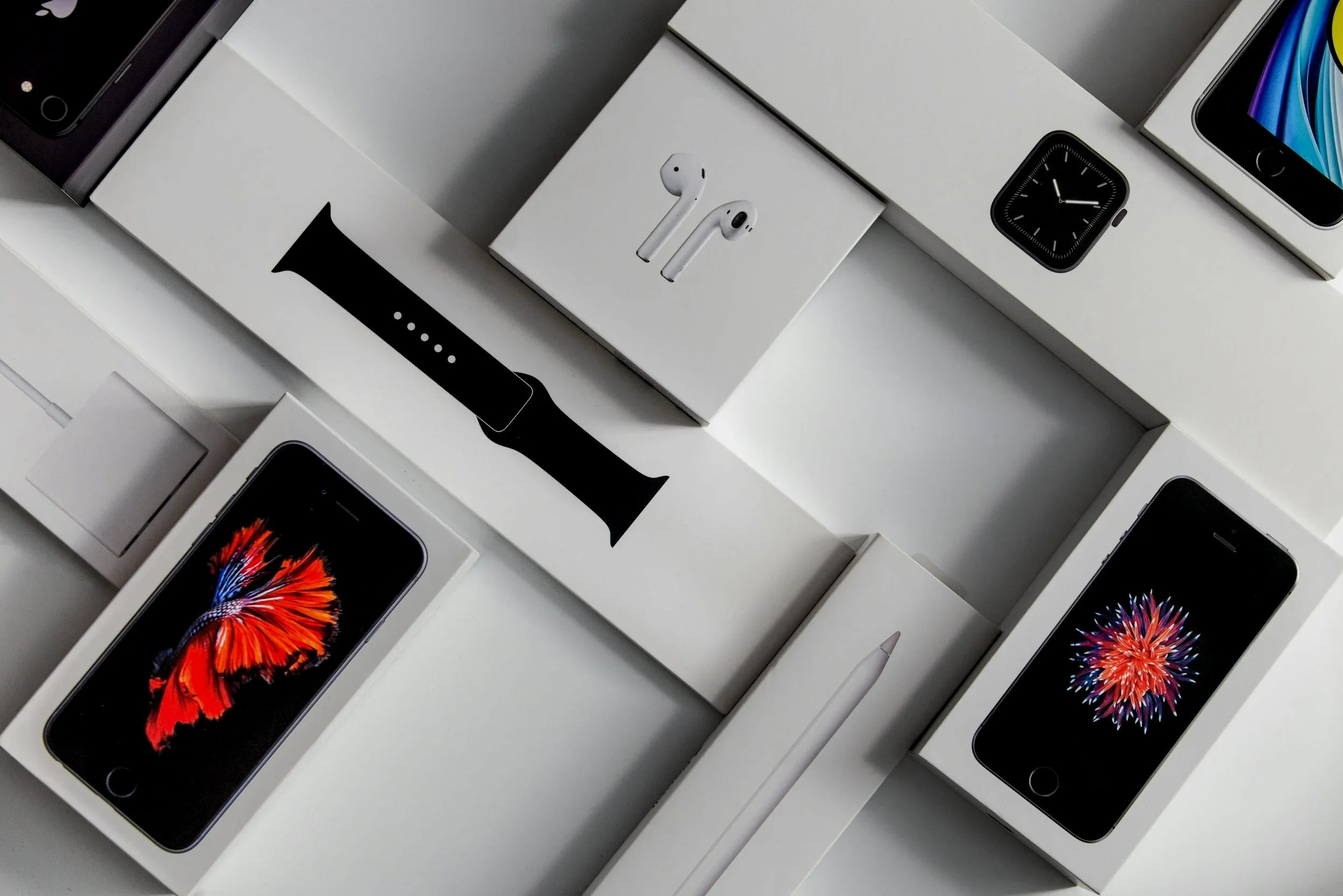 Multiple iPhone boxes and Apple Watch boxes stacked on top of each other, with one box open showing an iPhone with a colorful display and another displaying Apple AirPods.