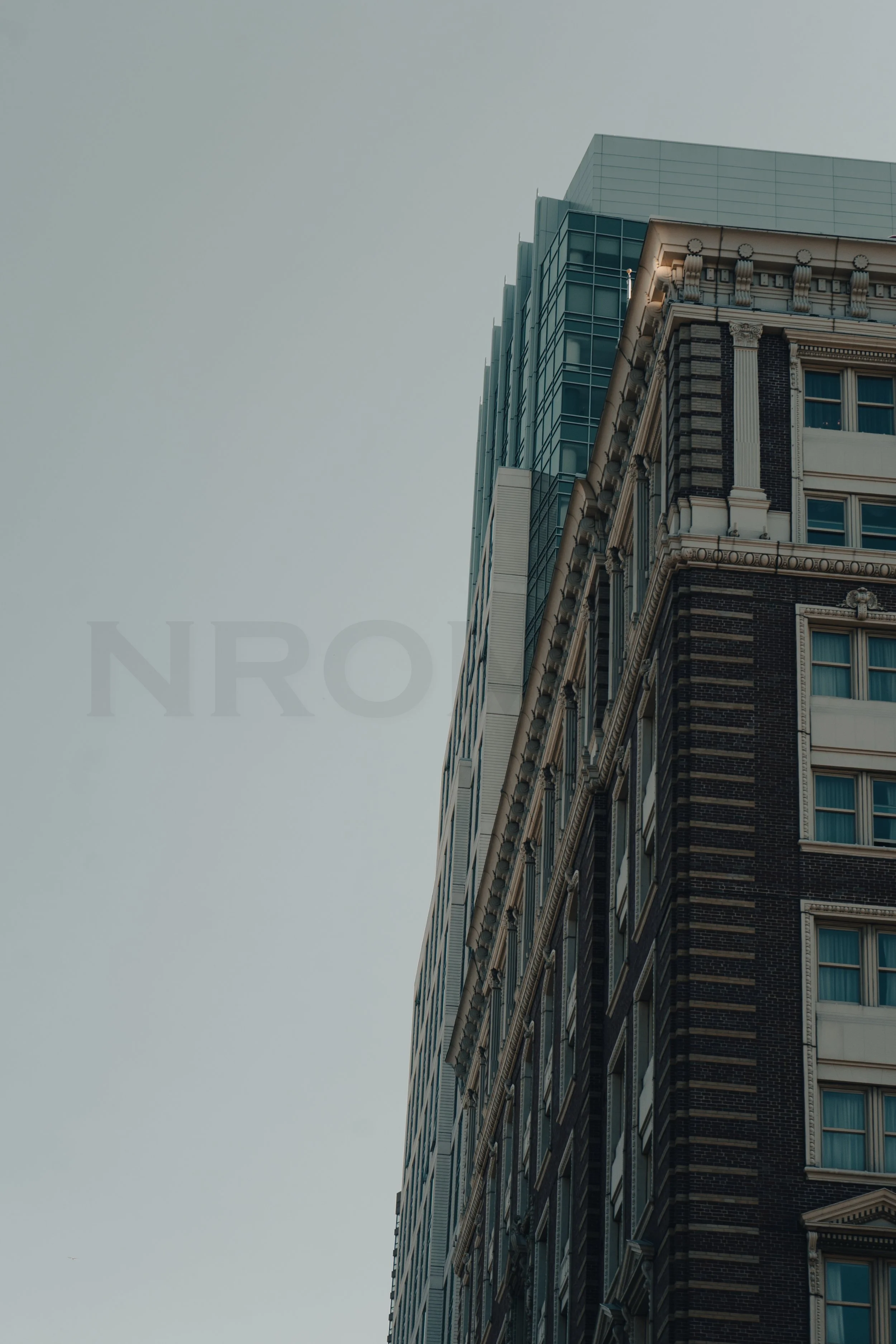 Close-up of tall modern and historic buildings against a gray sky, with the word 'NRO' faintly visible in the background.