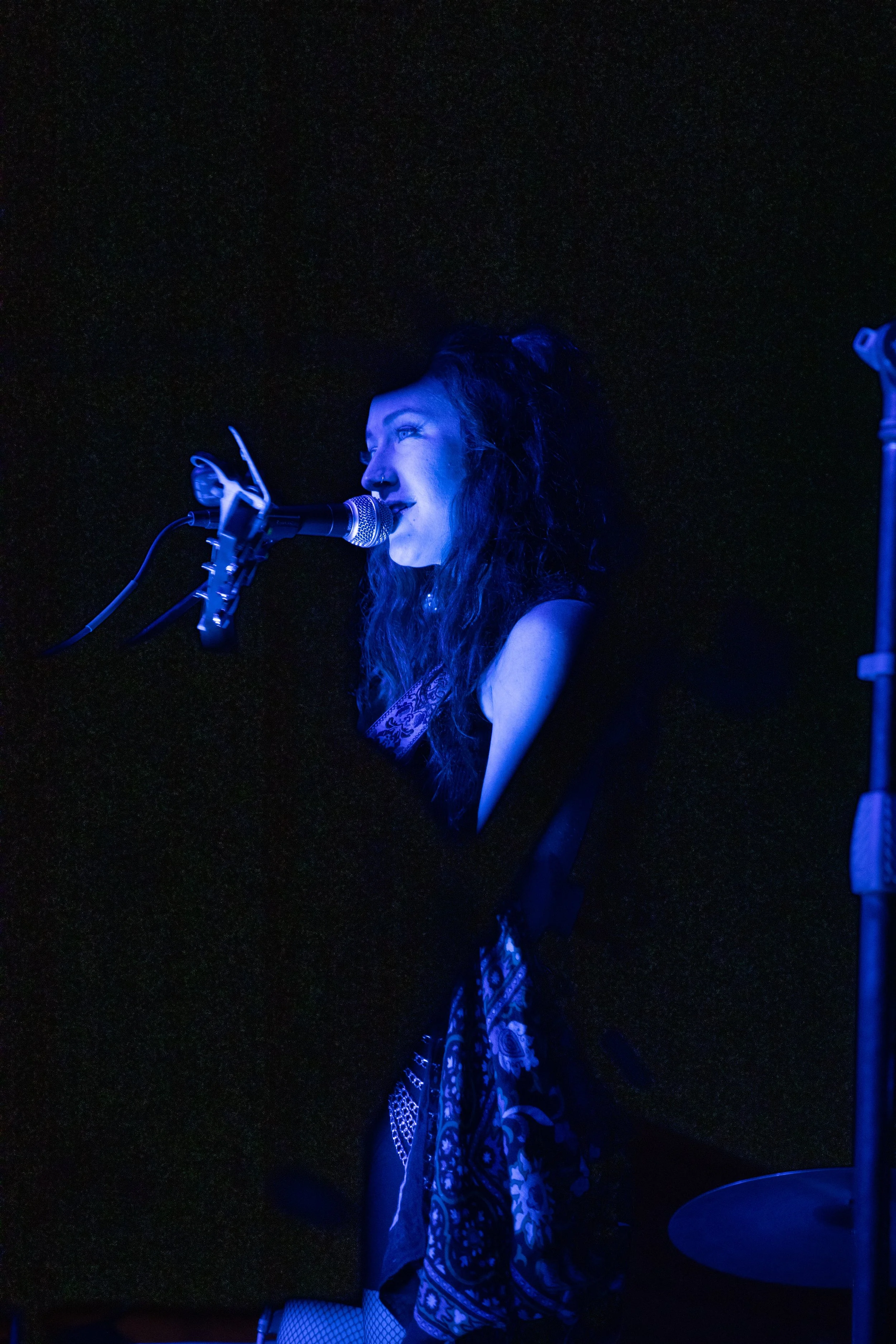 A woman singing into a microphone on stage under blue lighting.