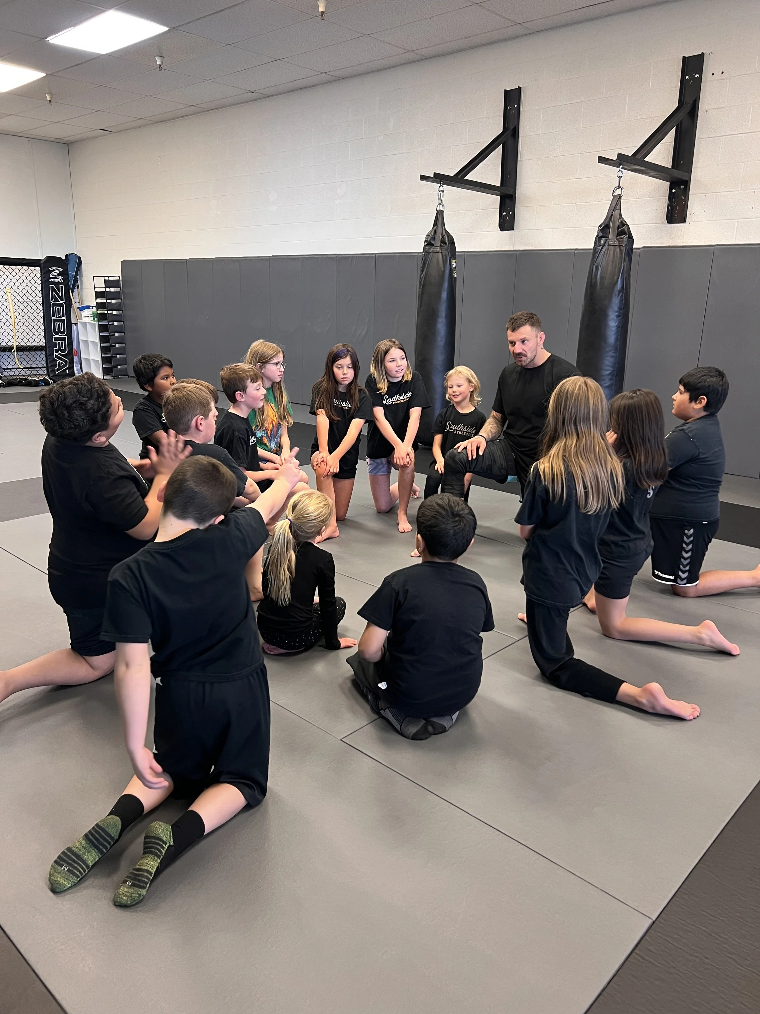 Coach Ben explaining a martial arts move to the Young Warriors program with kids taking a knee