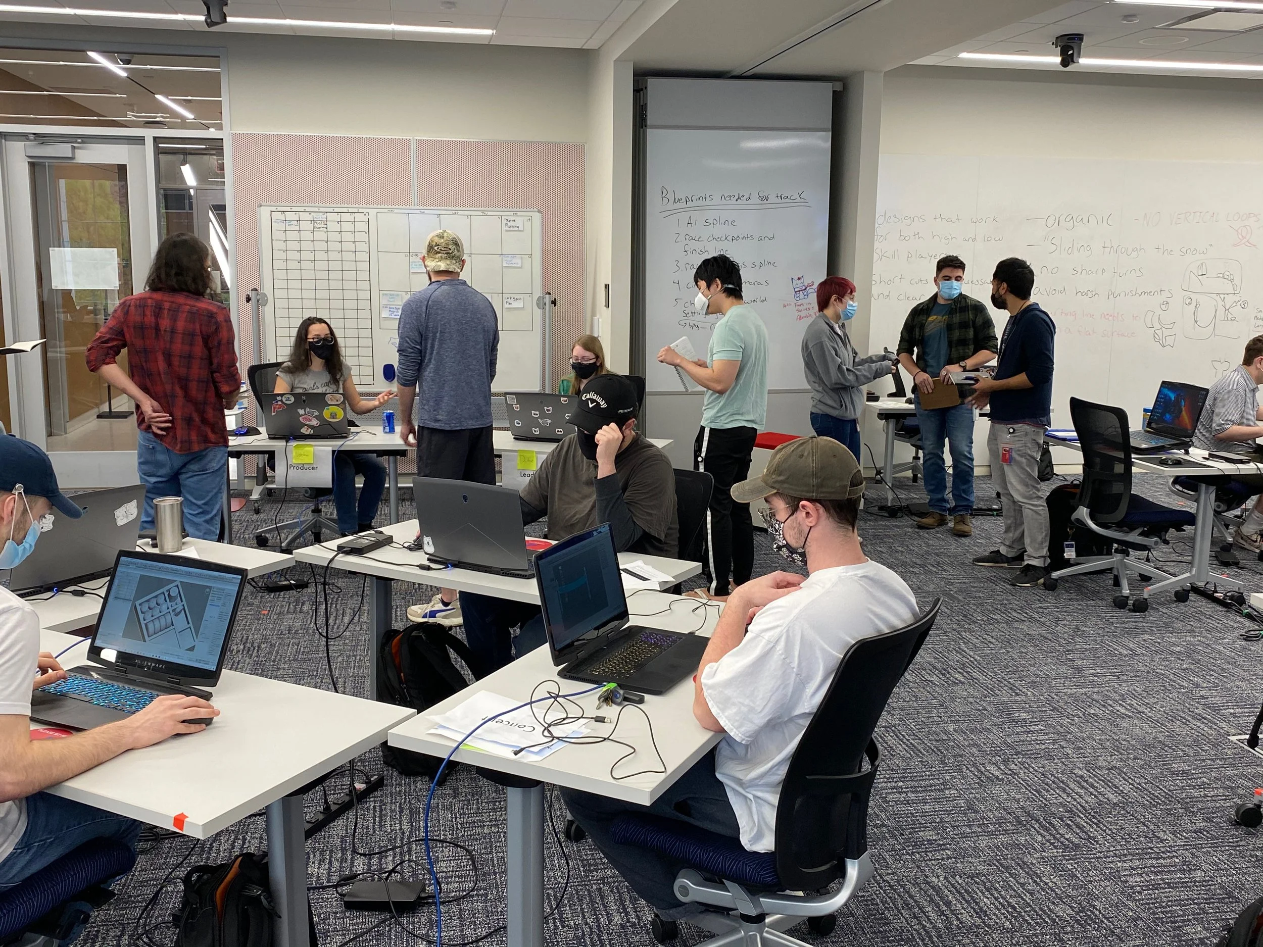 Photograph of Kam and Dakota speaking with Nooka and Dube at their desks. In the foreground, three artists are working at their computers.
