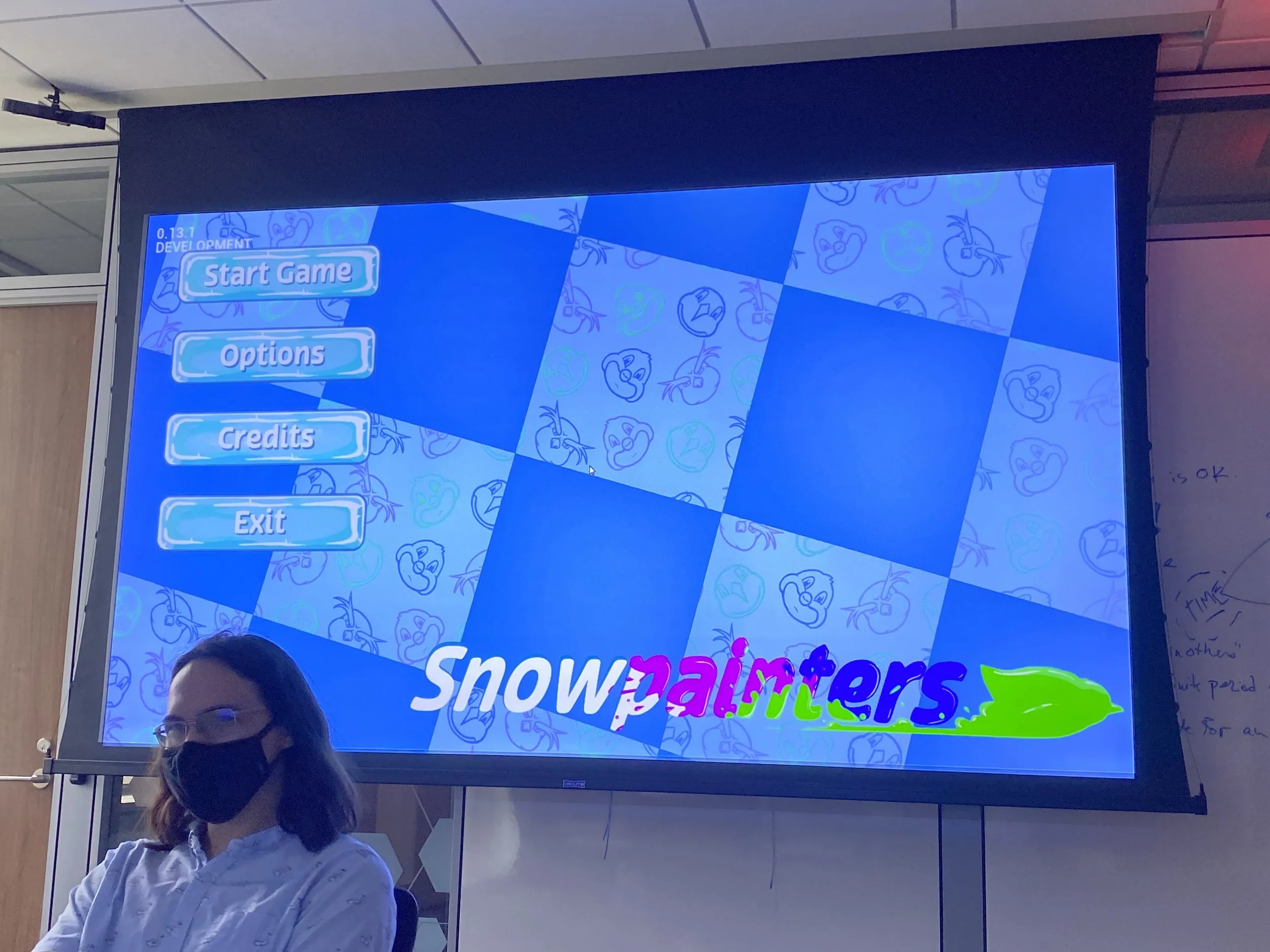Photograph of Kam sitting in front of a presentation of the game's start menu UI.