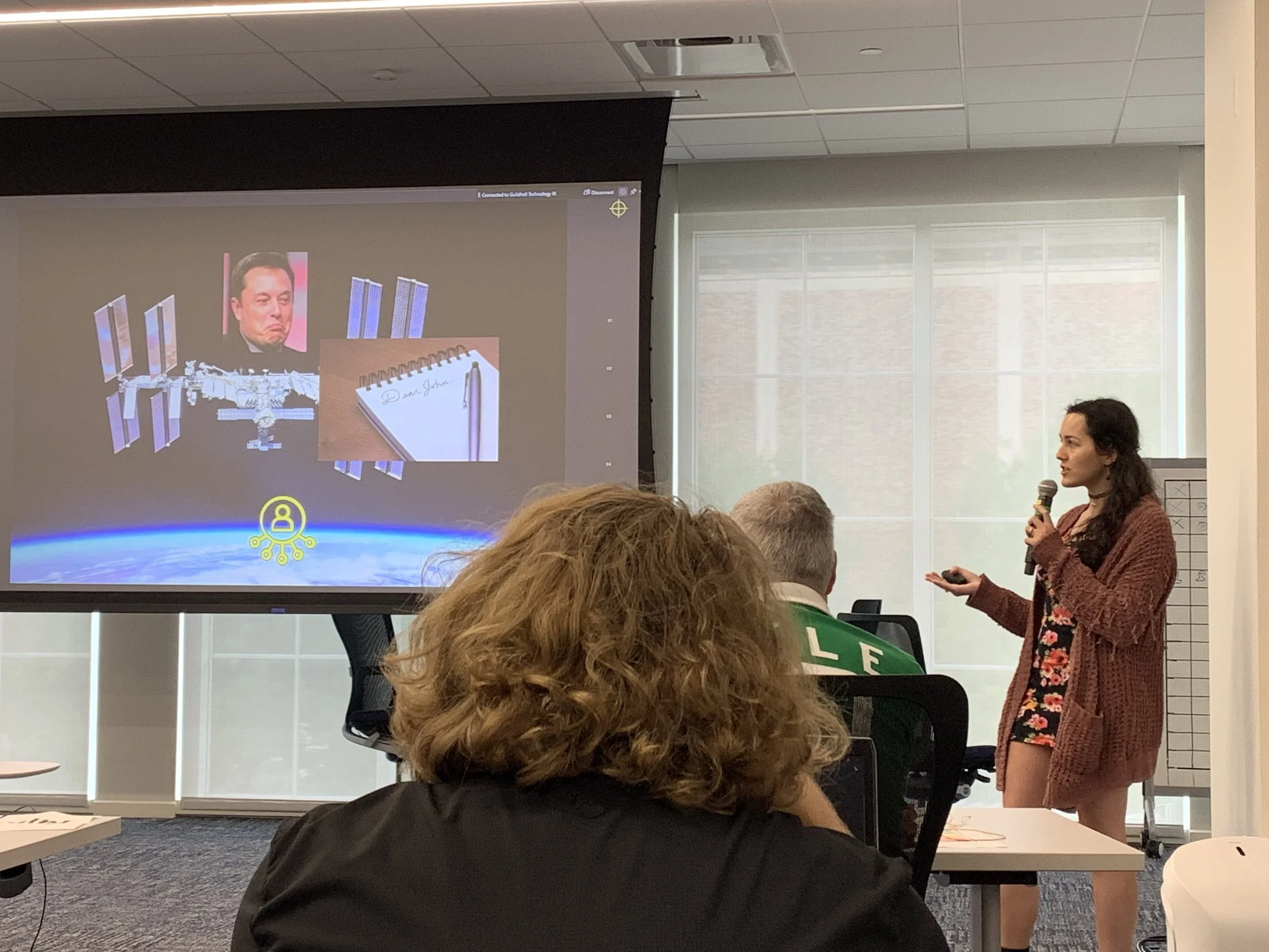 A photo of Nooka holding a microphone and giving a presentation.